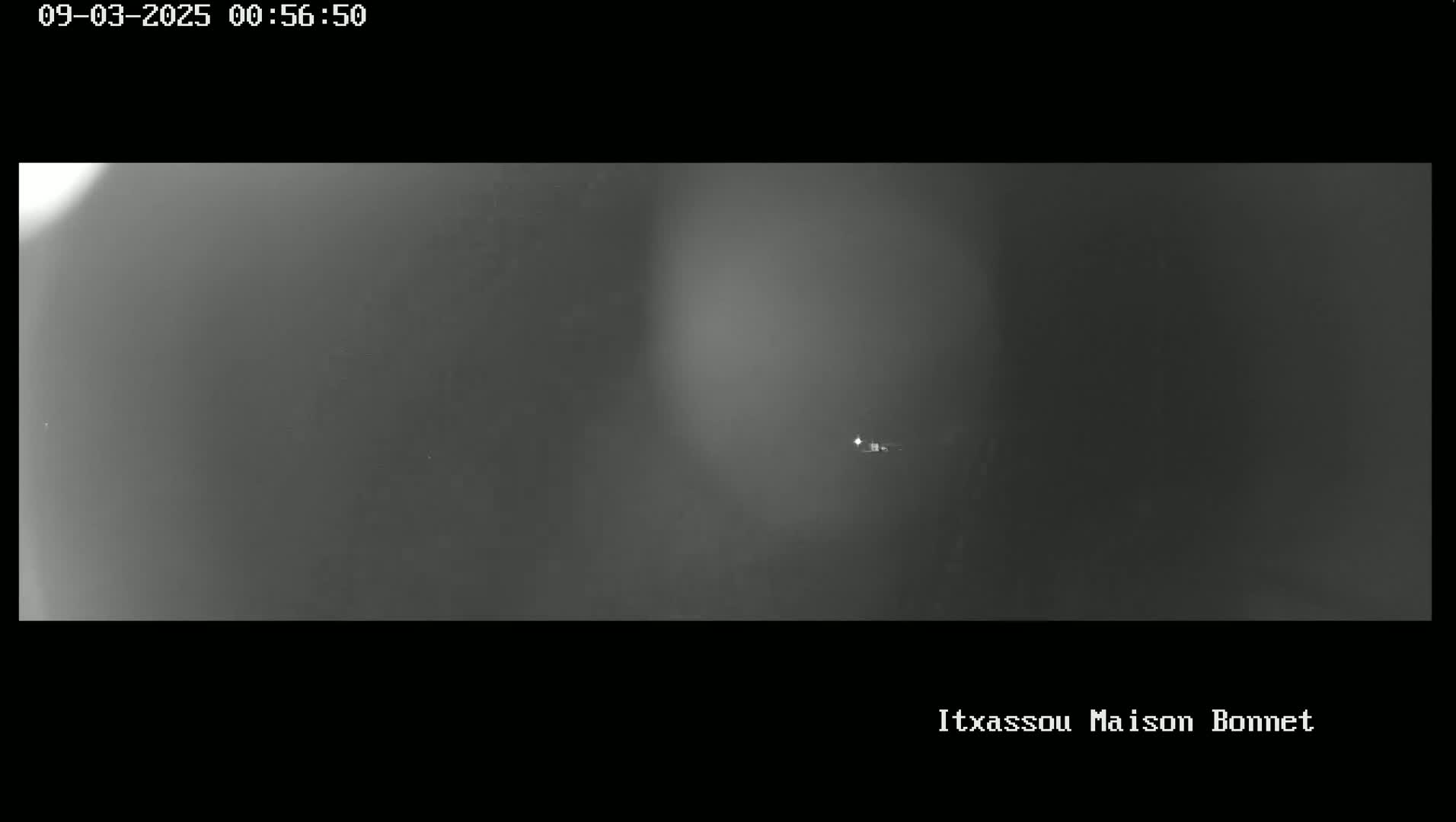 A nighttime, low-light image shows a dark, hazy sky with a single, small light source in the distance.