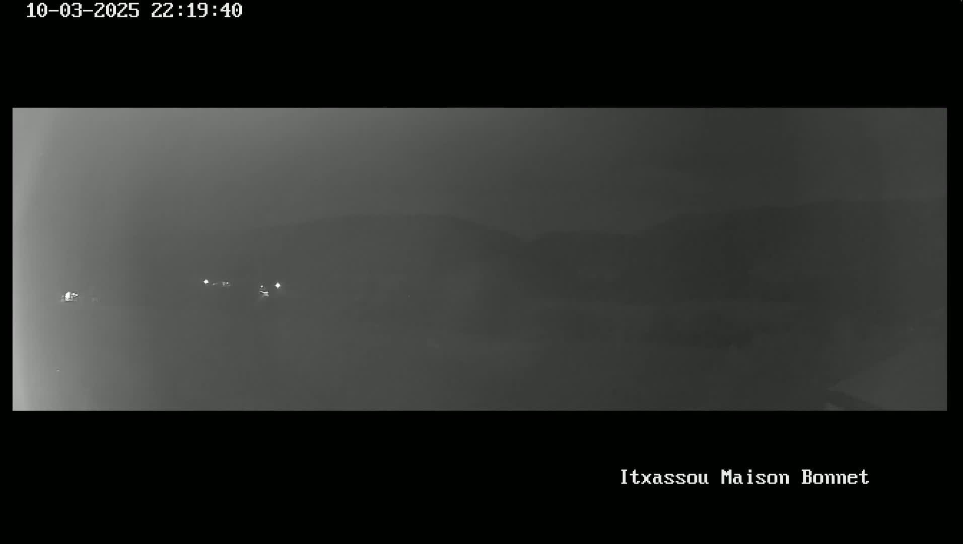 A nighttime, hazy view of dimly lit hills and a few distant lights.