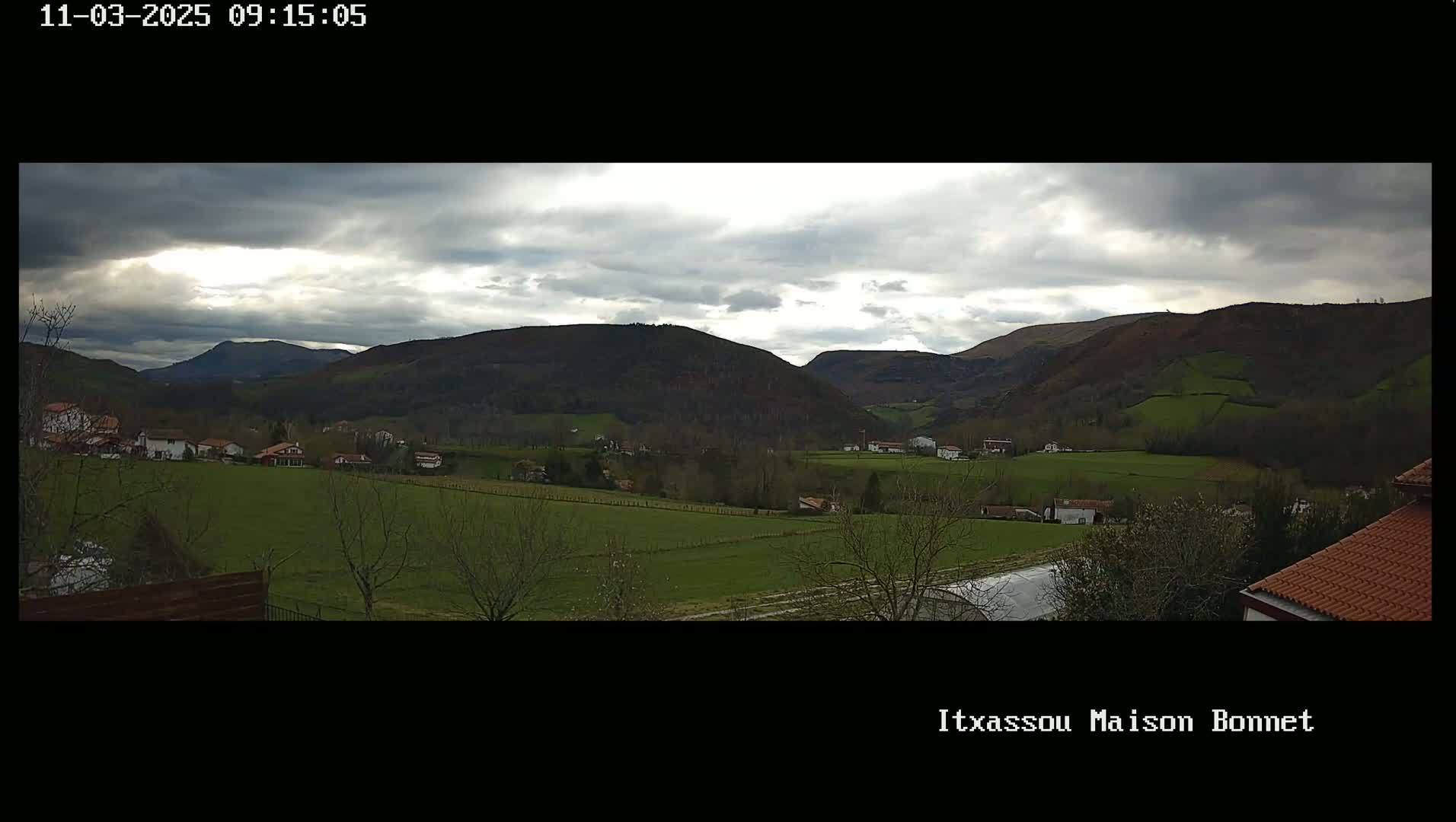 A sprawling green valley dotted with houses and farmlands, nestled between rolling hills under a cloudy sky.
