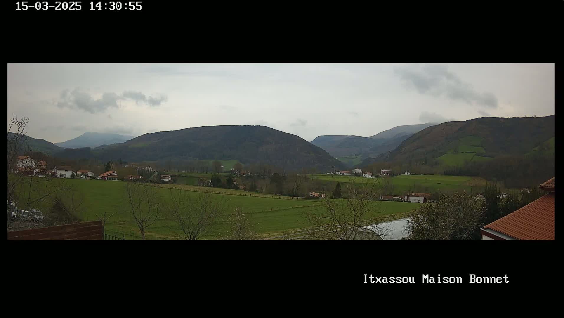 A panoramic view shows a valley with green fields and scattered houses under a cloudy sky.