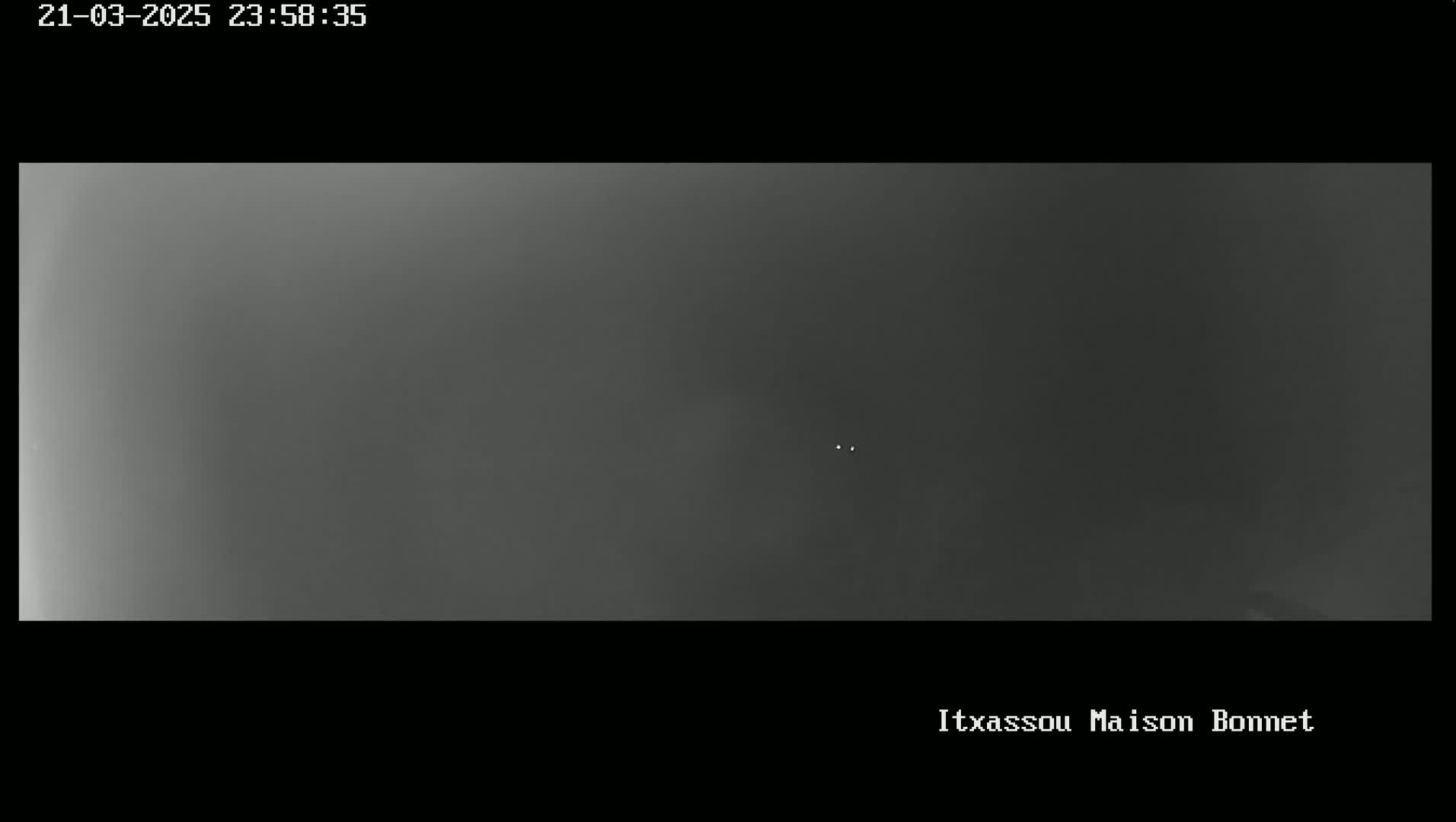 A grainy, dark gray image shows a dimly lit, possibly nighttime outdoor scene with very low visibility.