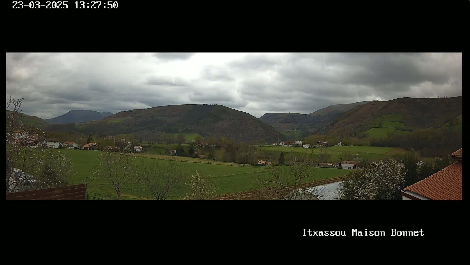A rural valley with overcast skies, dotted with houses and farmland, is nestled between rolling hills.