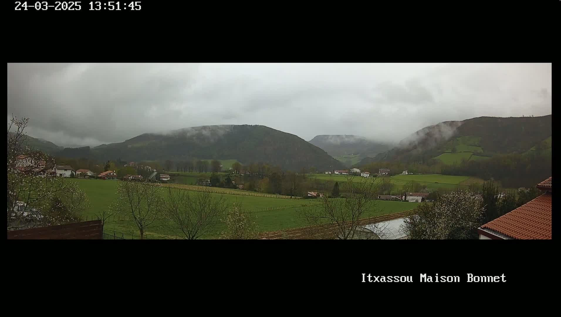 A misty, overcast day reveals a verdant valley dotted with houses and farmland, nestled against rolling hills.