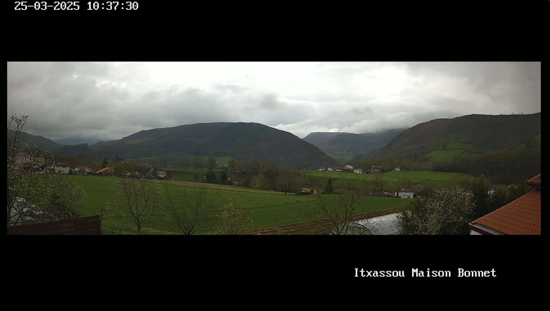 A cloudy day reveals a pastoral valley scene with rolling green hills, farmland, and a few houses nestled amongst the trees.
