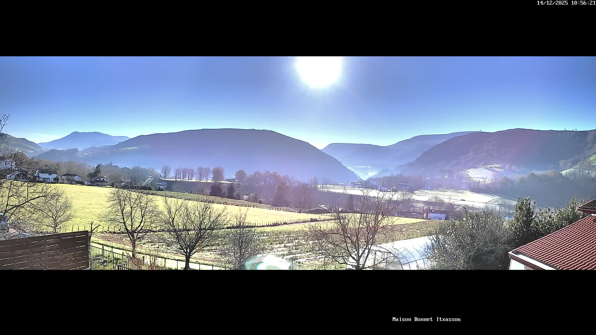 A wide panoramic view captures a rural valley dotted with houses and green fields surrounded by tree-covered hills under a heavily overcast and gloomy sky.