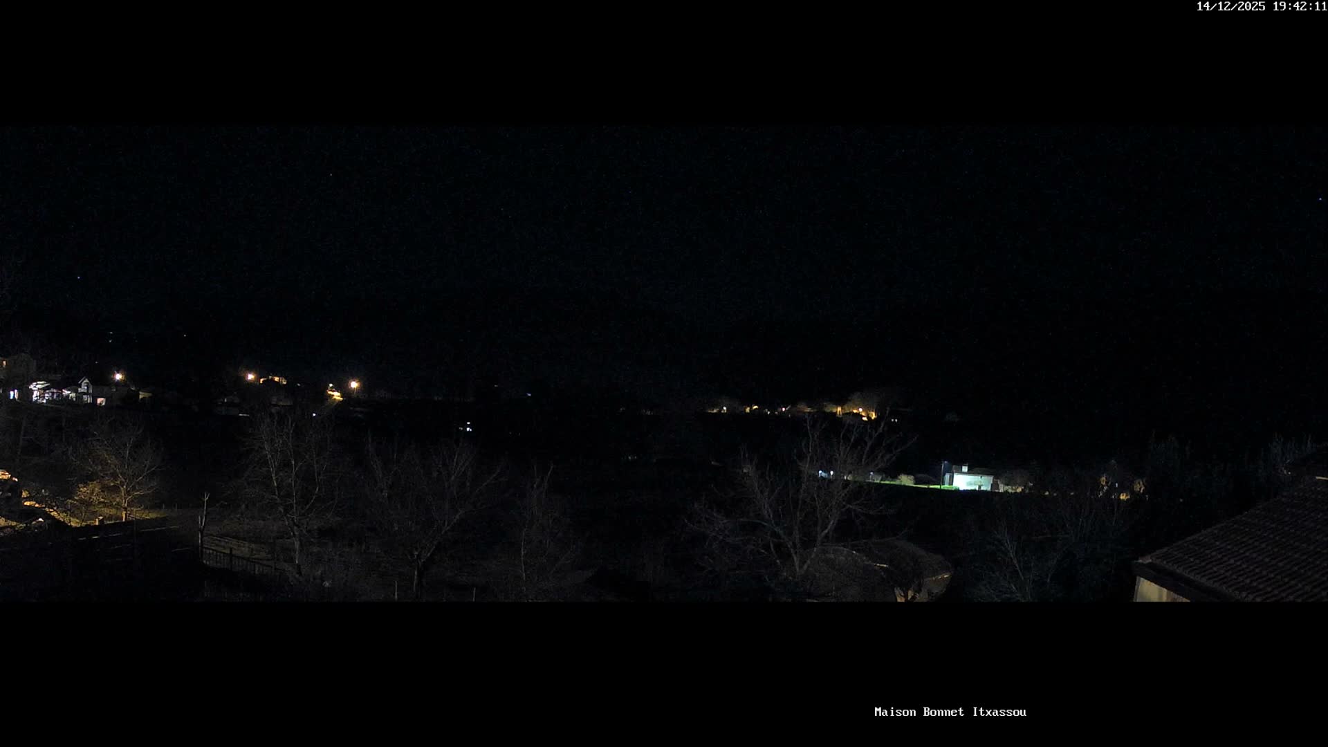 A wide panoramic view captures a rural valley dotted with houses and green fields surrounded by tree-covered hills under a heavily overcast and gloomy sky.