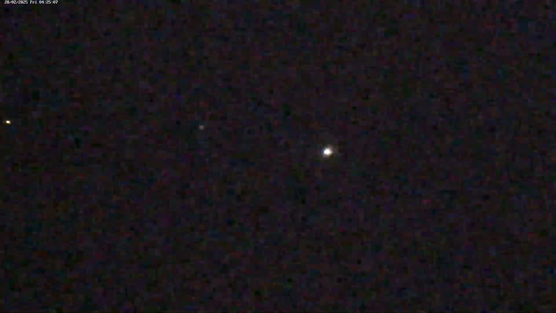 A nighttime image shows a bright light, possibly a planet or star, in the center with fainter lights visible in the distance under a clear, dark sky.