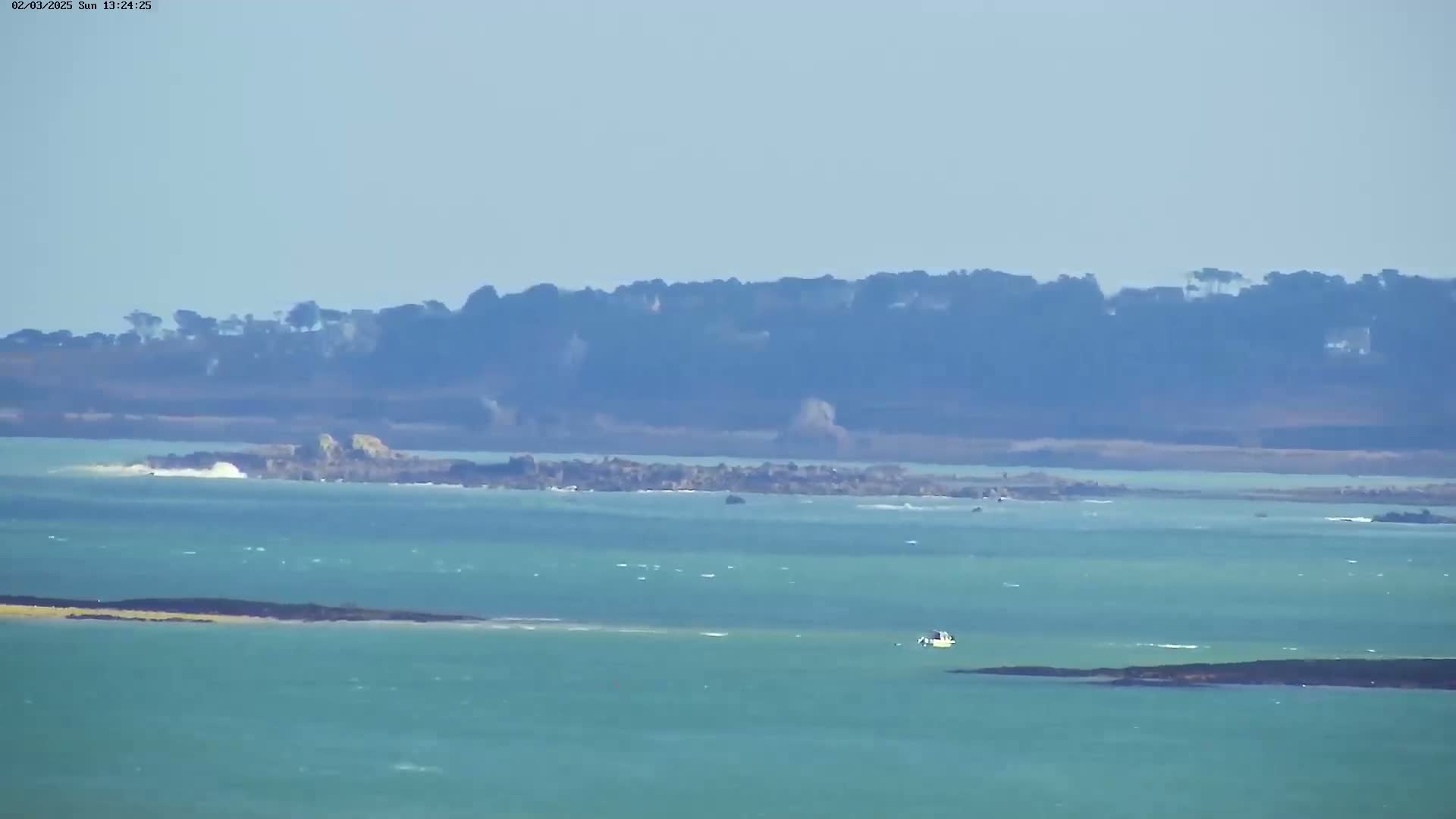 A small boat is visible on a body of teal-colored water, with a distant shoreline of dark green trees and rocky outcrops under a clear sky.