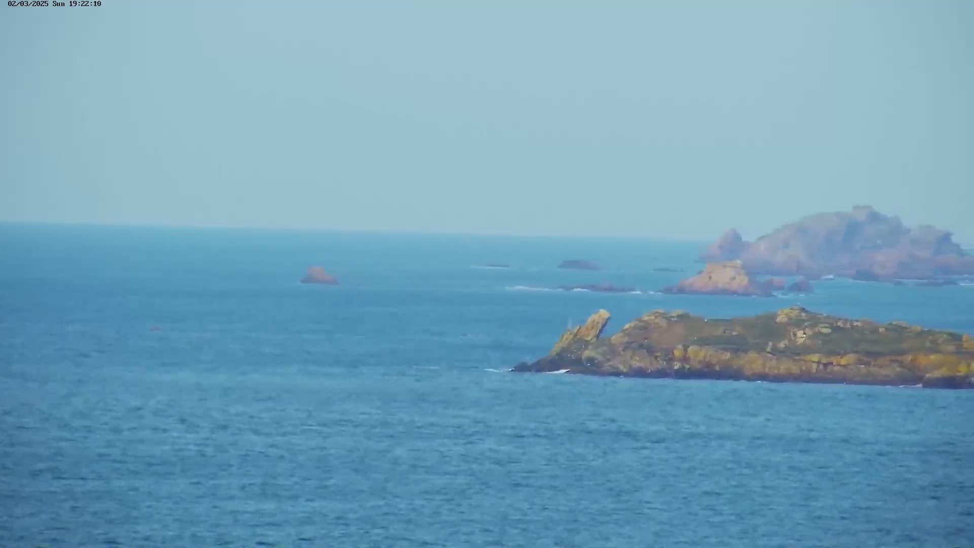 A wide, calm ocean view shows several rocky islands and islets under a clear, light-blue sky.