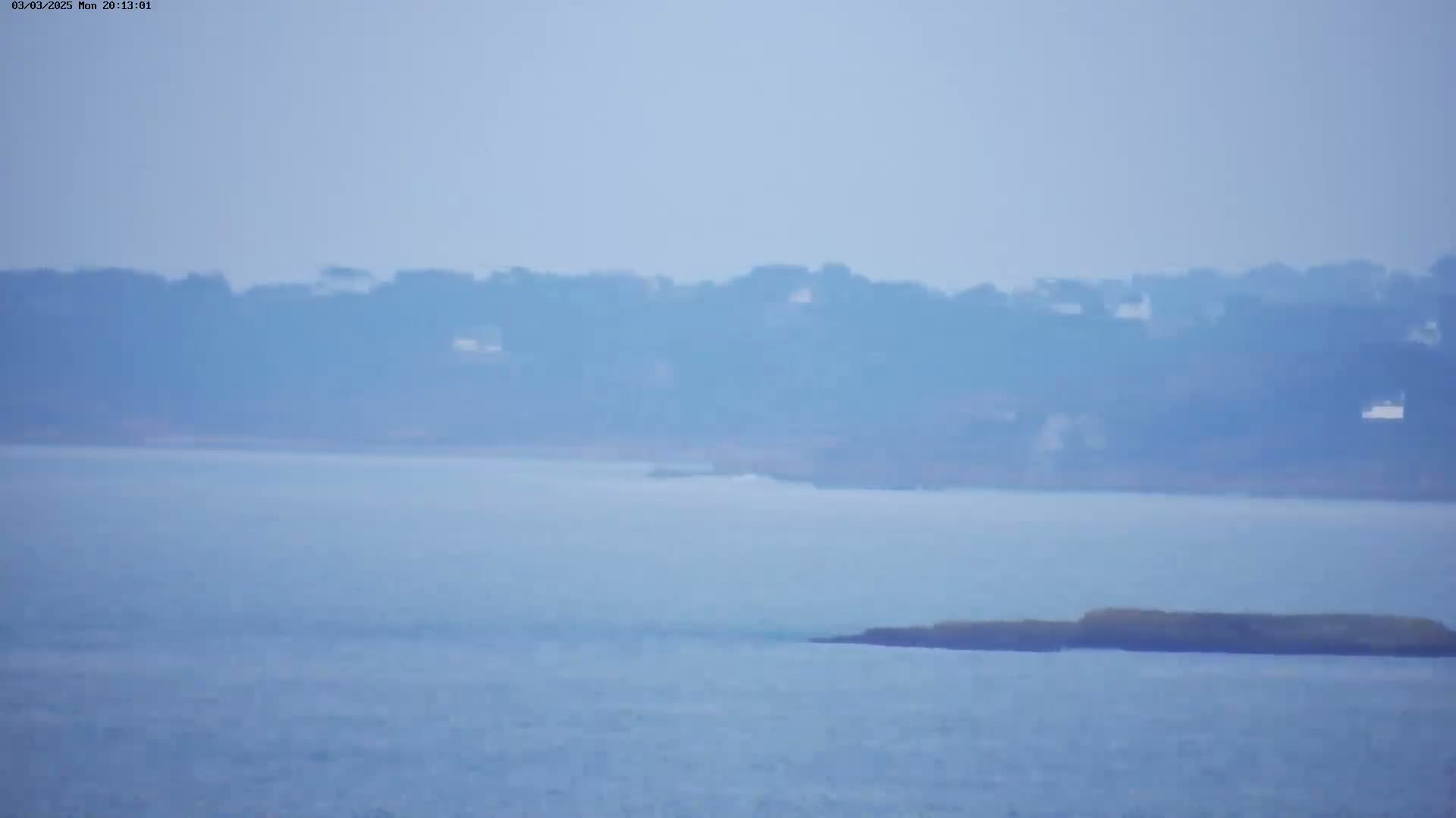 A hazy, light-blue body of water stretches out to a distant shoreline of muted trees and buildings.