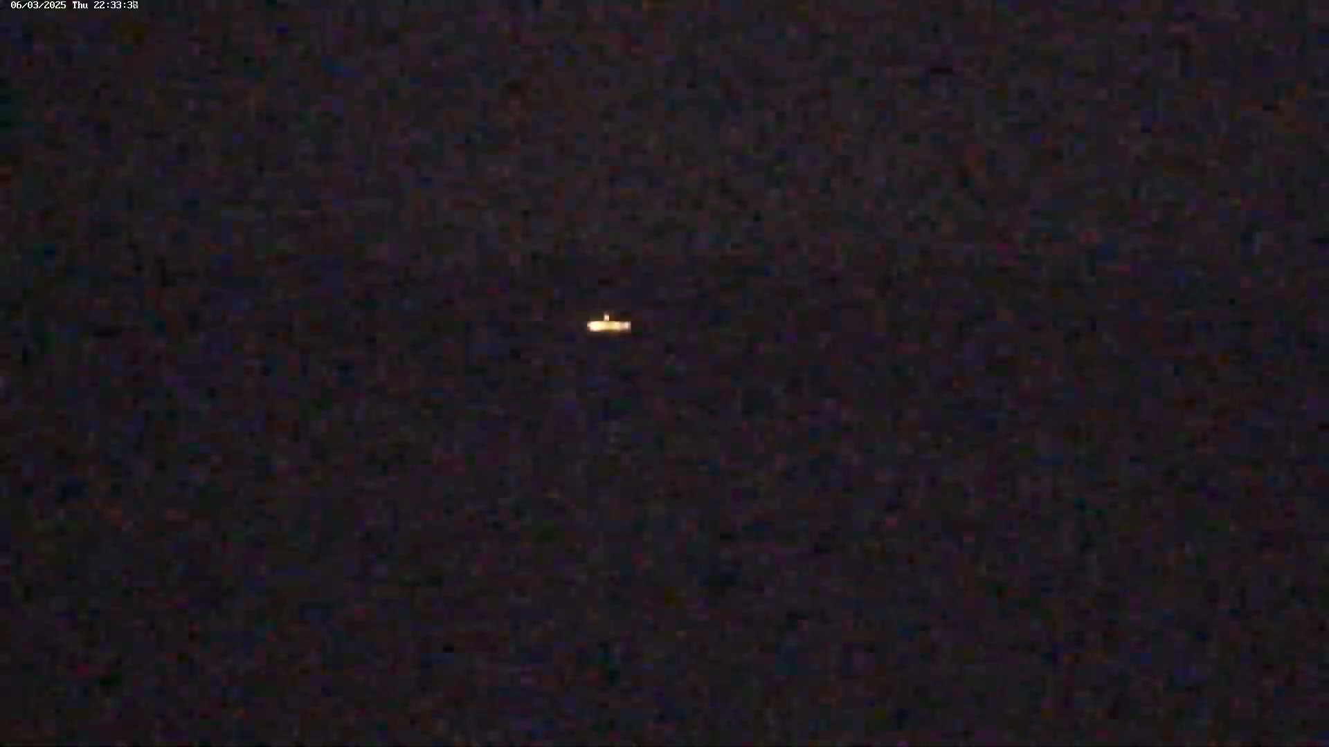 A small, faint light is visible in a dark, nighttime sky.