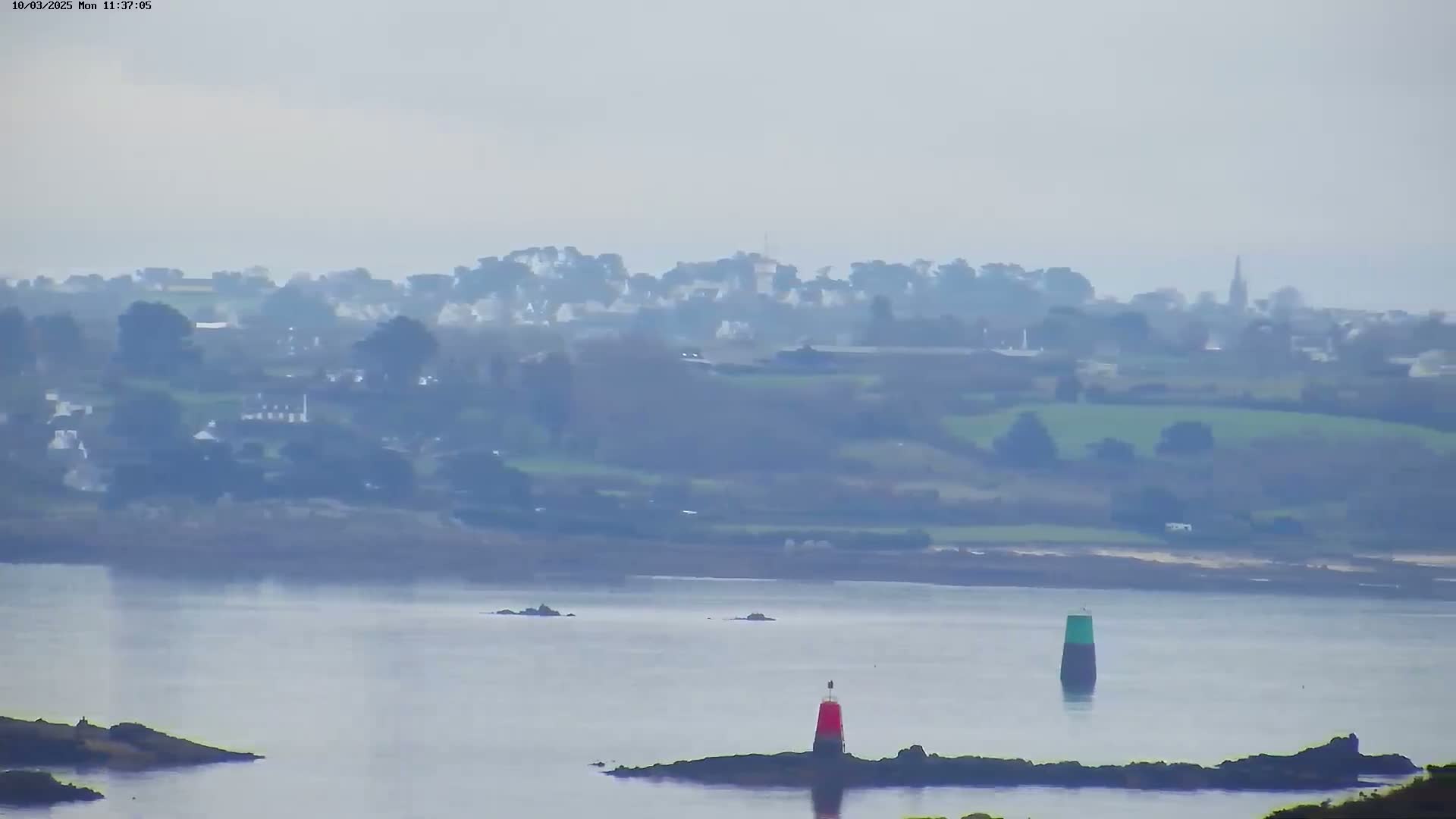A hazy, distant view of a coastal town and waterway, featuring two small navigational markers in the foreground.