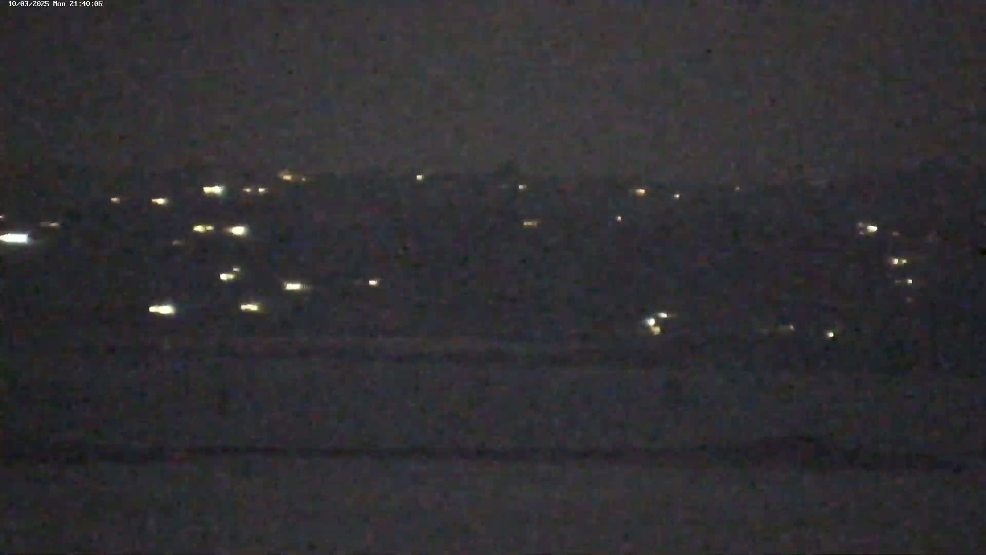 A nighttime long shot of a distant town's scattered lights under a dark, possibly overcast sky.