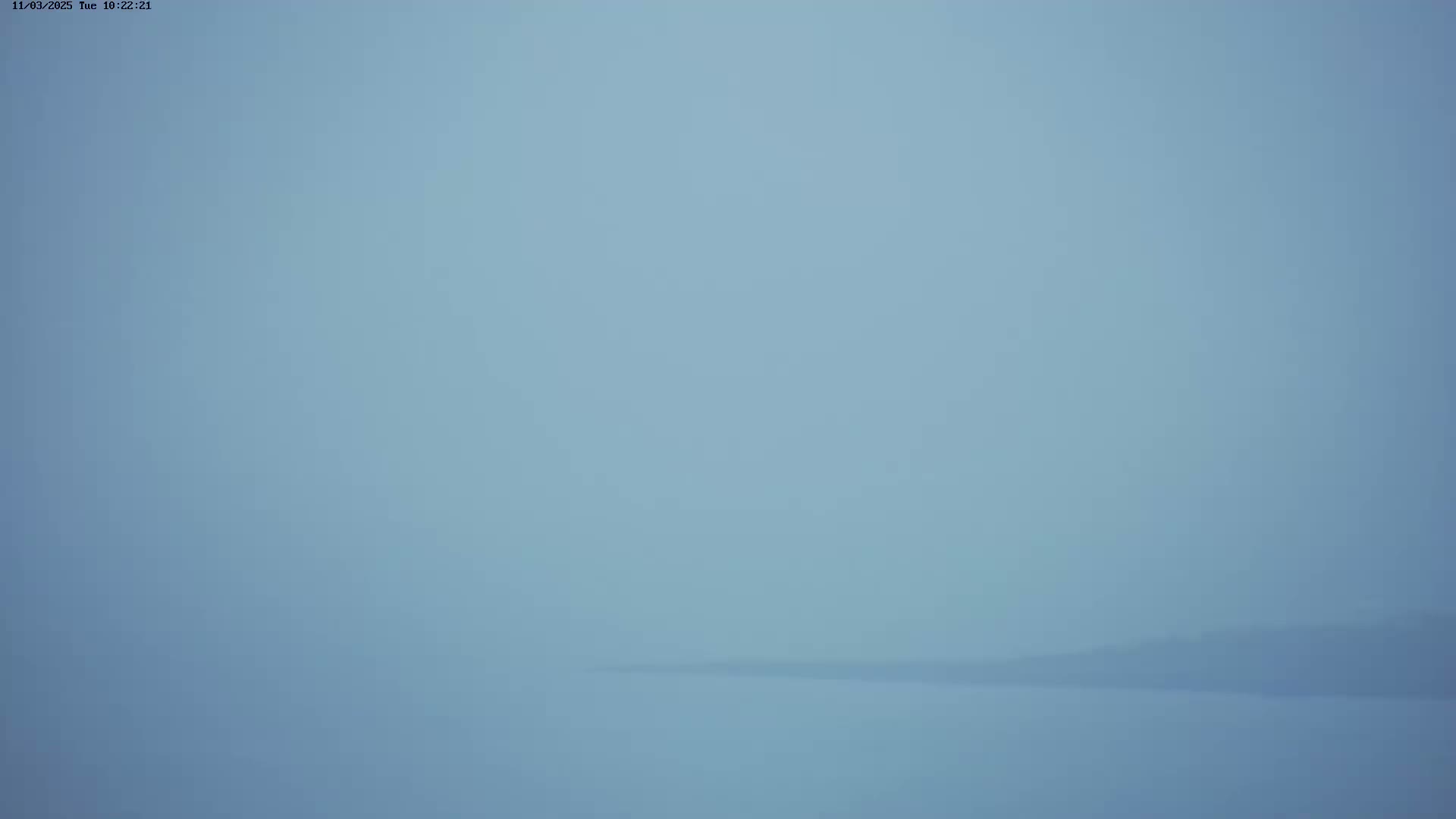 A hazy, light-blue landscape shows a barely visible horizon line where land meets a body of water under a foggy sky.