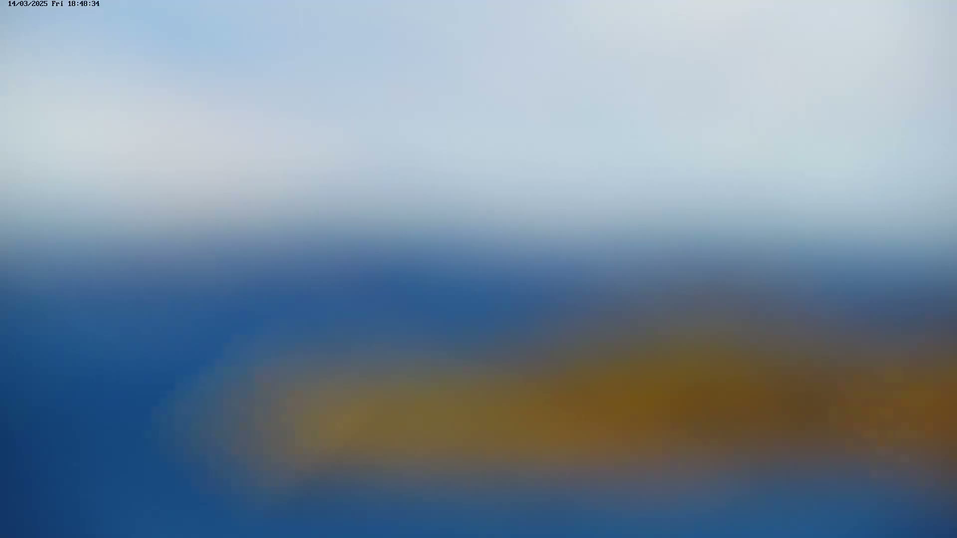 A blurry image shows a mostly blue landscape with a horizontal band of brownish-yellow in the lower middle, under a light blue sky.