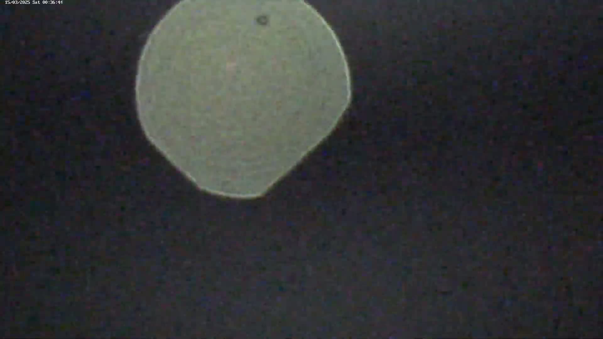 A pale, off-white, irregularly-shaped object is centered against a dark, nighttime sky.