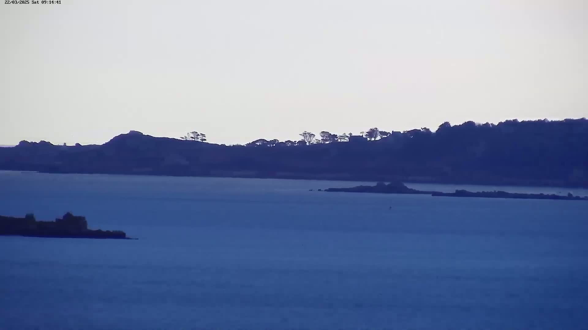 A calm body of water stretches out before a distant shoreline, silhouetted against a pale sky.