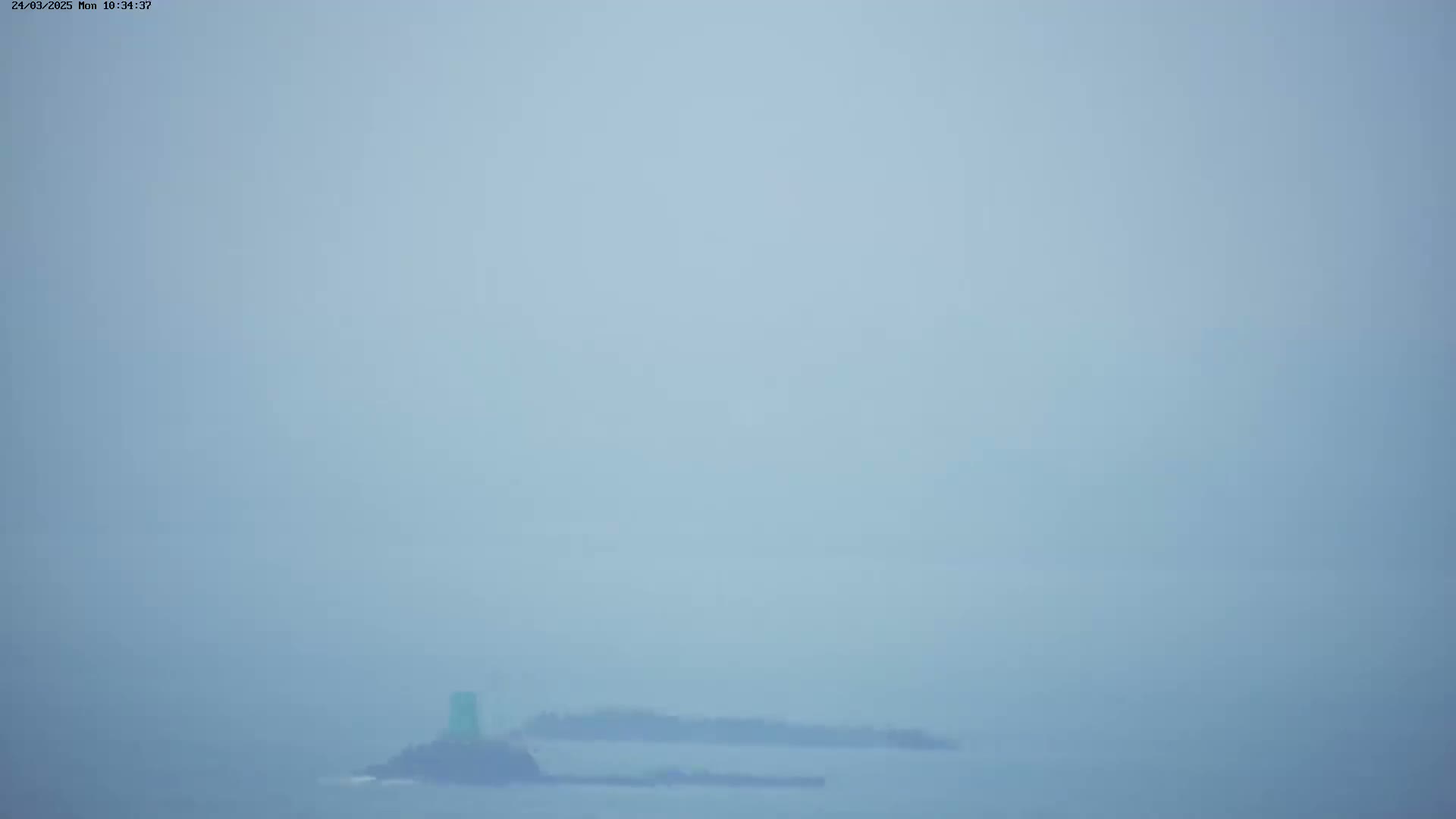 A hazy, foggy view of a small island with a light green structure visible in the distance over a body of water.