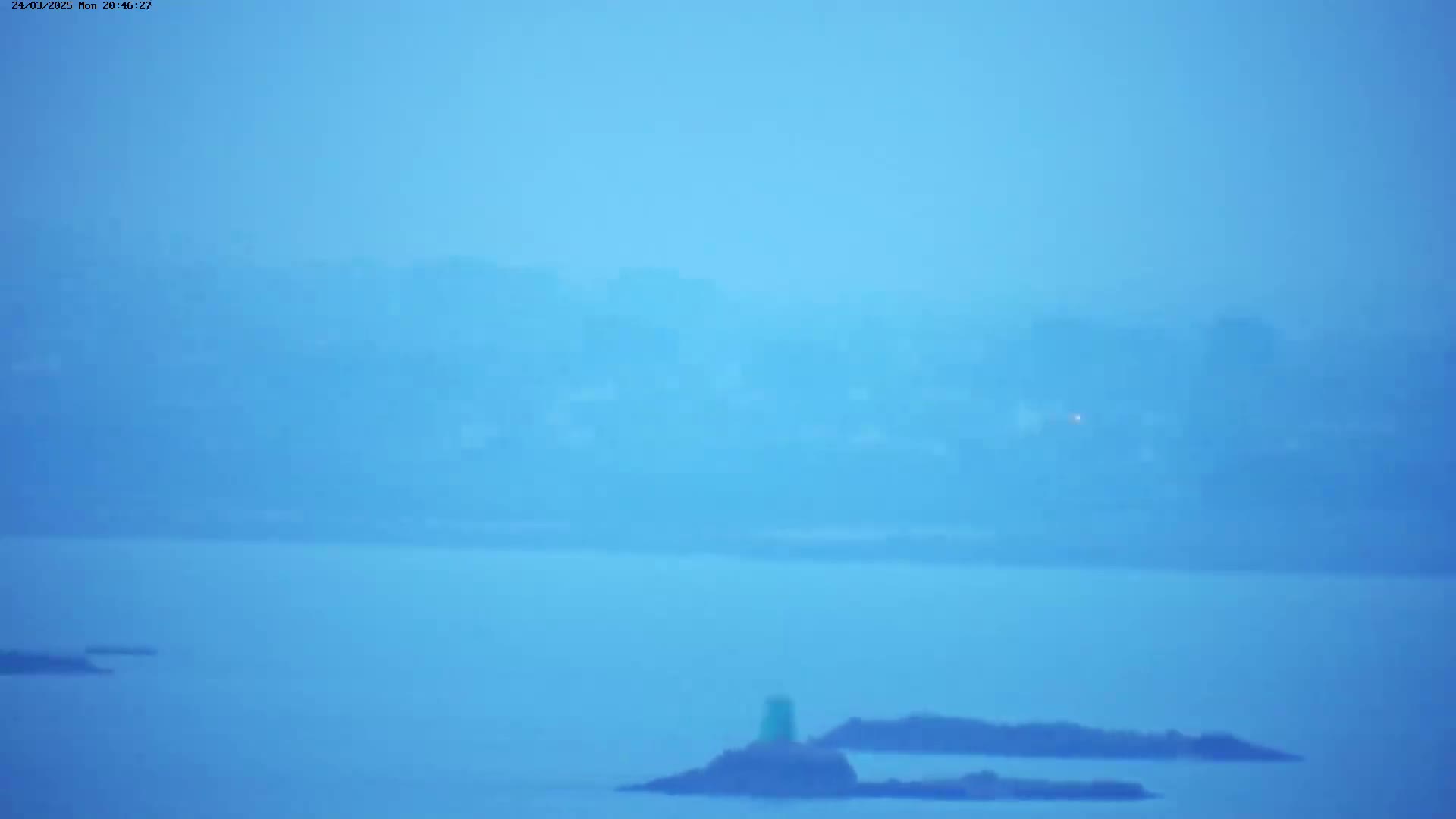 A hazy, light-blue view shows a body of water with small islands and a distant, indistinct shoreline.