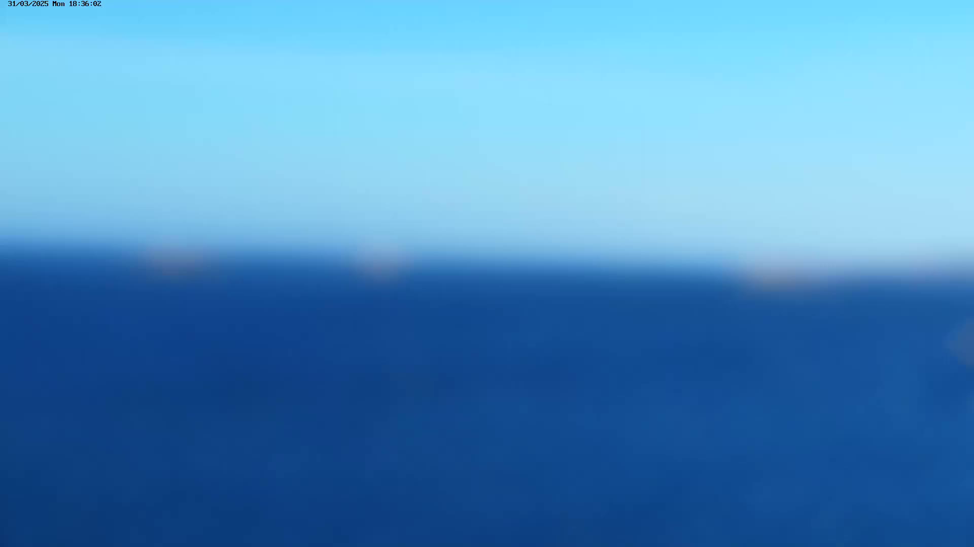 A blurry image shows a blue sky above a dark blue body of water under clear conditions.