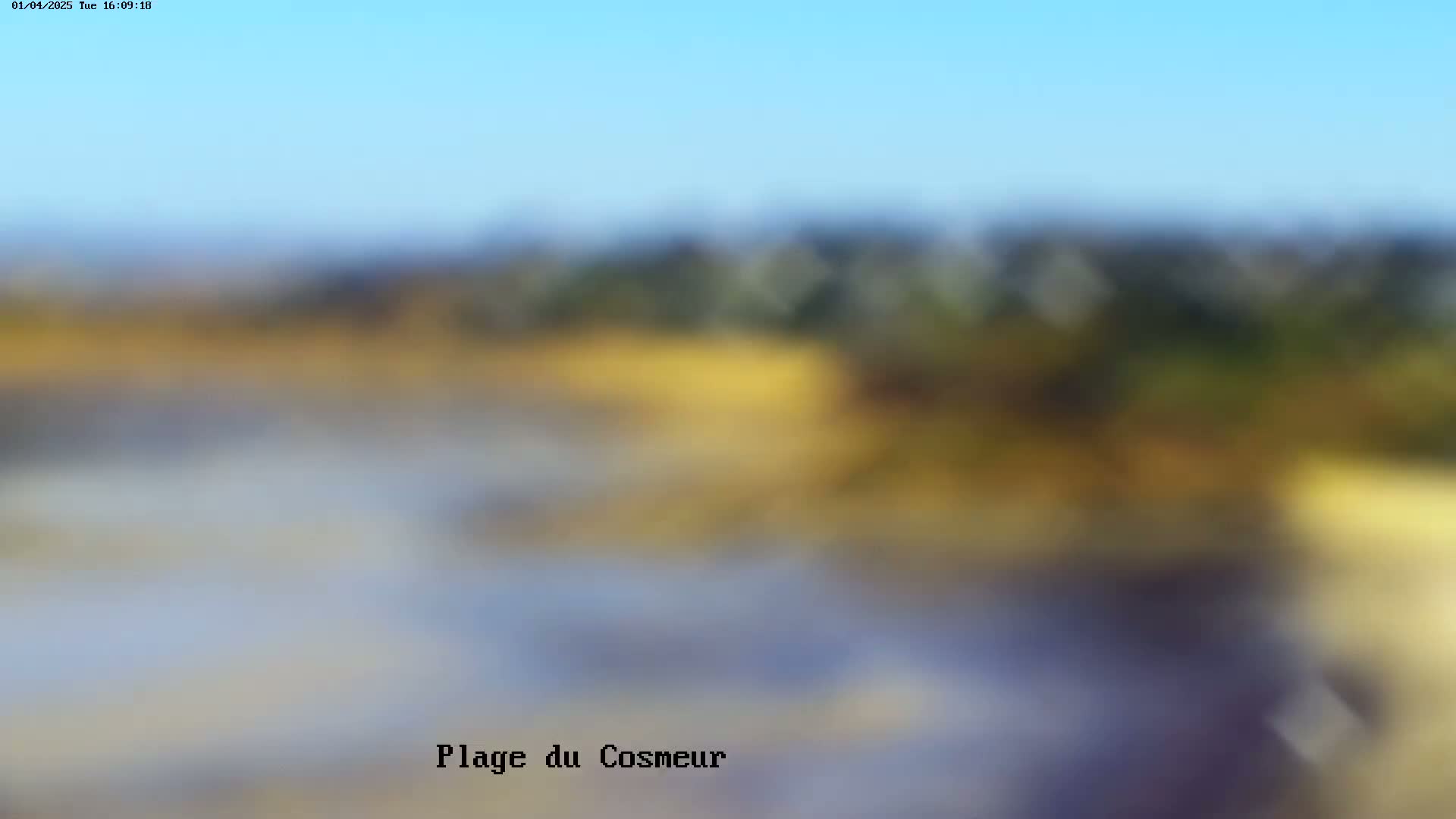 A blurry, out-of-focus image depicts a landscape under a clear blue sky, showing muted yellows, blues, and greens in the distance.