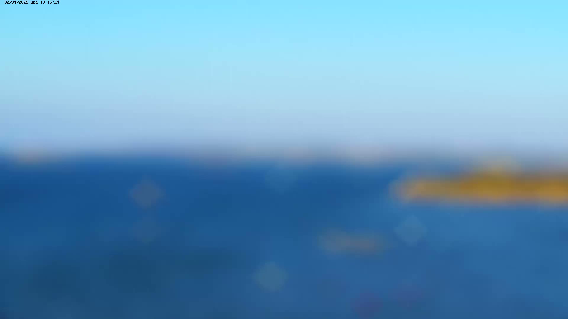 A blurry image shows a calm body of blue water under a clear, light-blue sky.