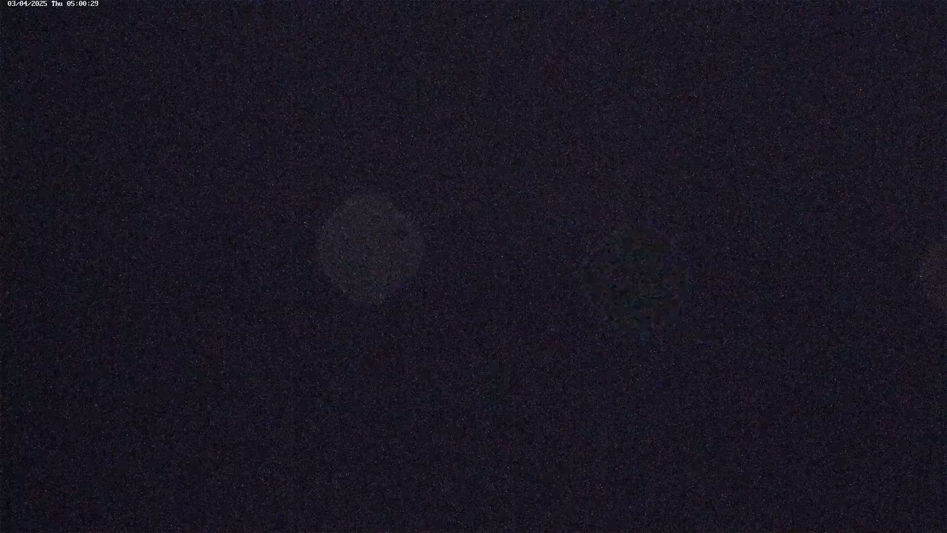 A dark, nighttime image shows two blurry, light-colored spots against a grainy, dark background.