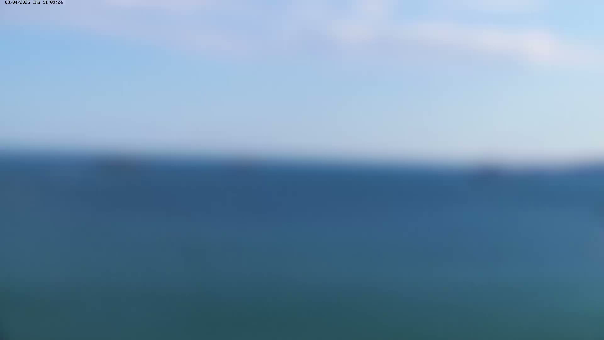 A blurry image shows a calm, blue ocean under a pale blue sky.