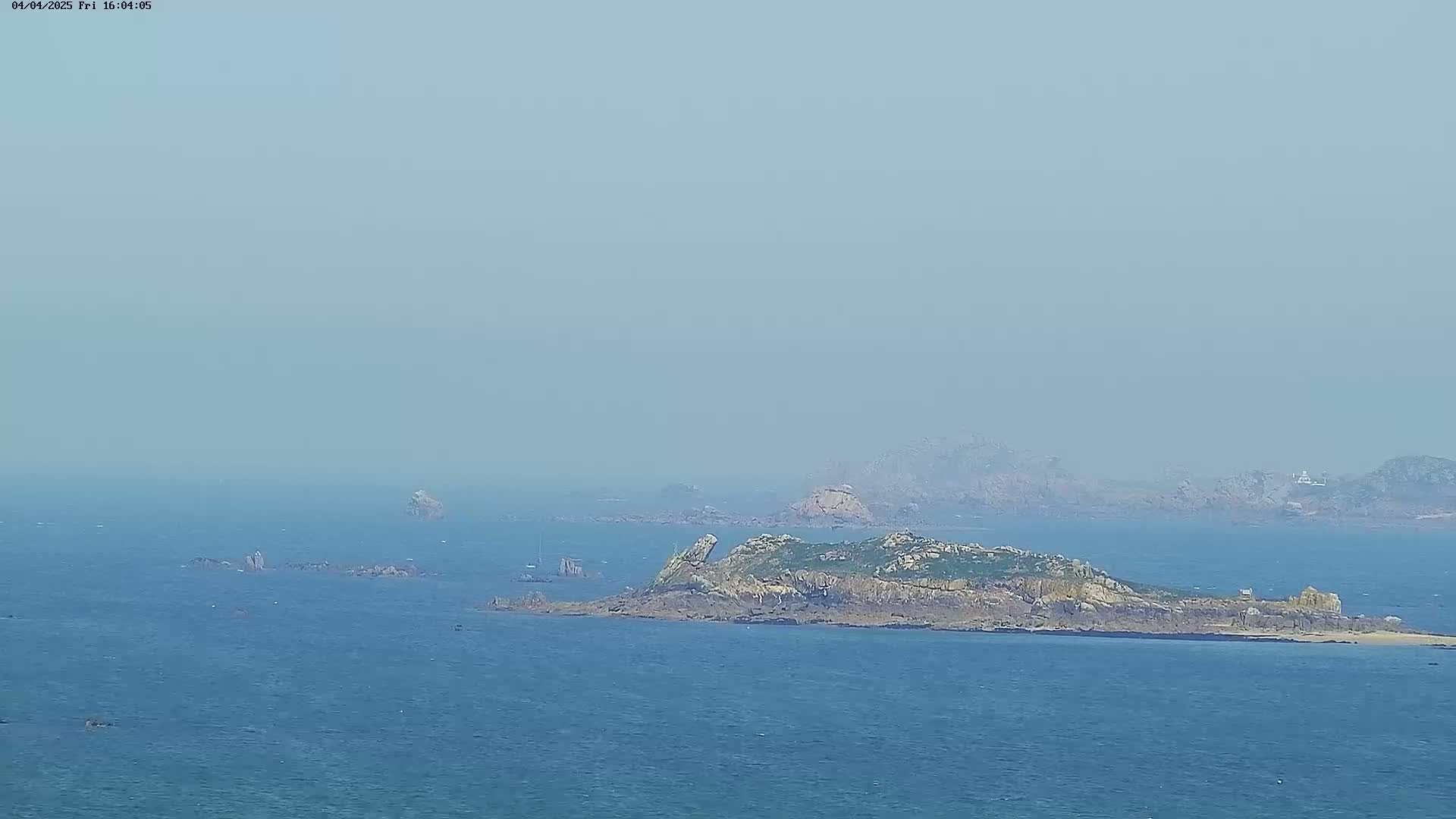 A hazy, long shot shows a rocky island and several smaller islets in a calm, blue sea.