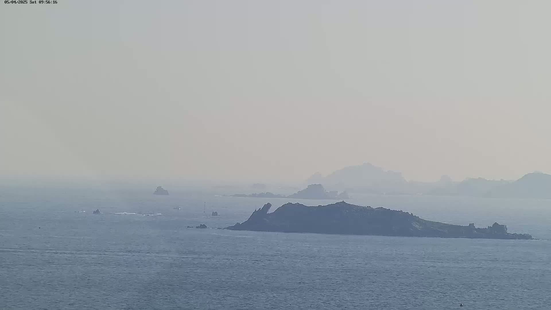 A hazy, distant view of several dark, rocky islands and smaller outcroppings in a calm sea.