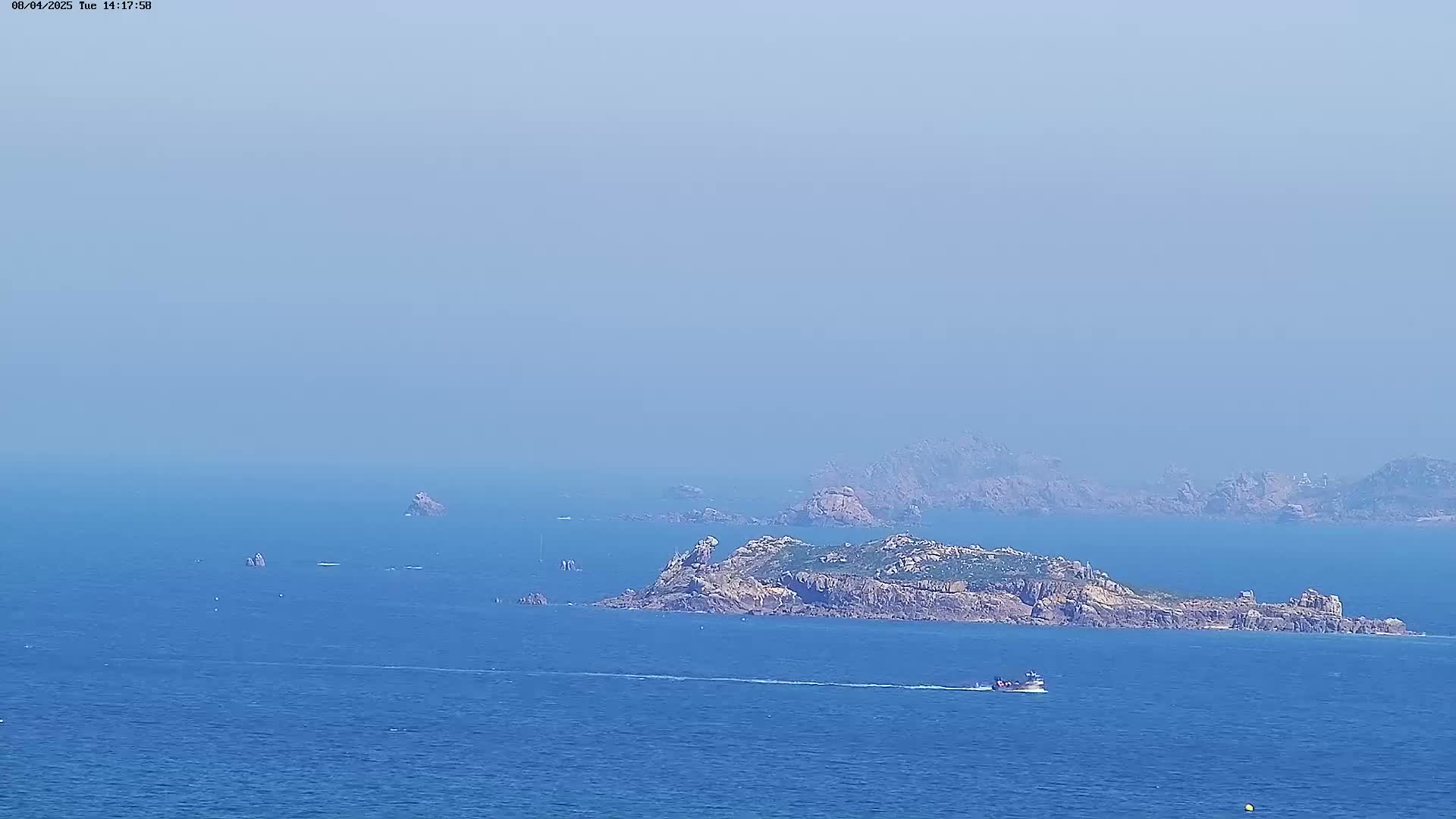 A hazy, blue ocean scene shows a small boat passing by a rocky island, with additional smaller rock formations and landmasses visible in the distance.