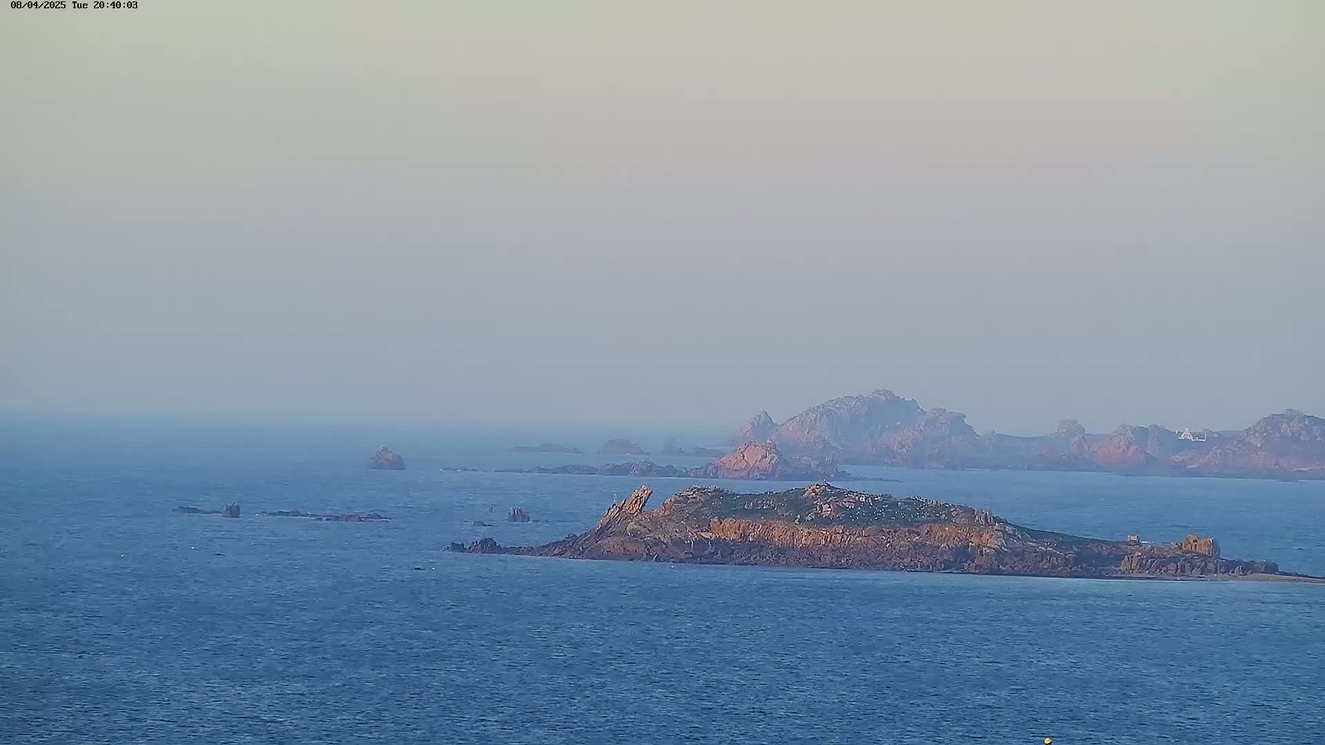 A hazy view of several rocky islands surrounded by calm blue ocean.