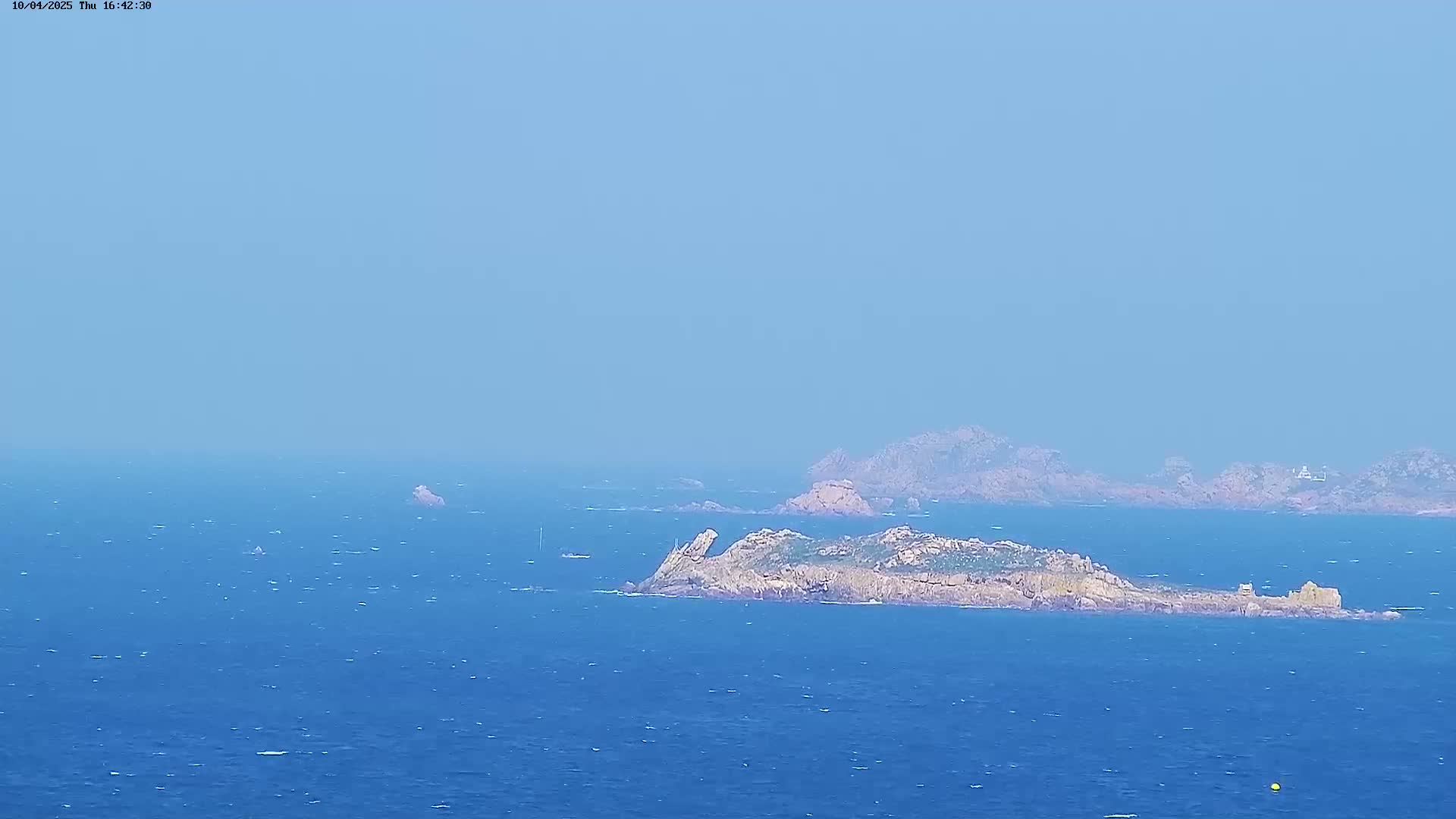 A hazy blue ocean stretches to the horizon, where rocky islands and a distant coastline are visible under a clear sky.