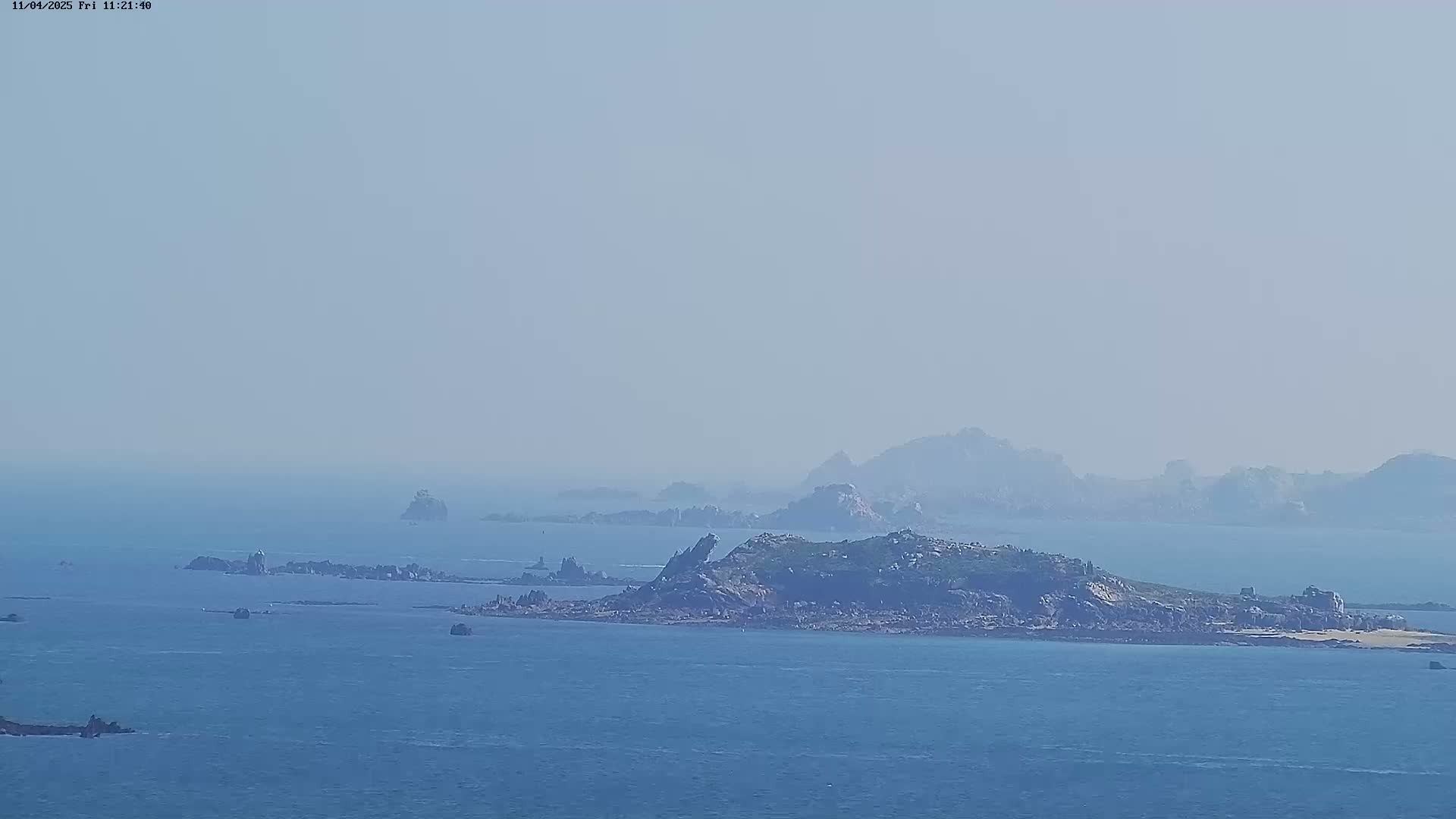 A hazy view of a rocky island and several smaller islets in a calm, blue sea.