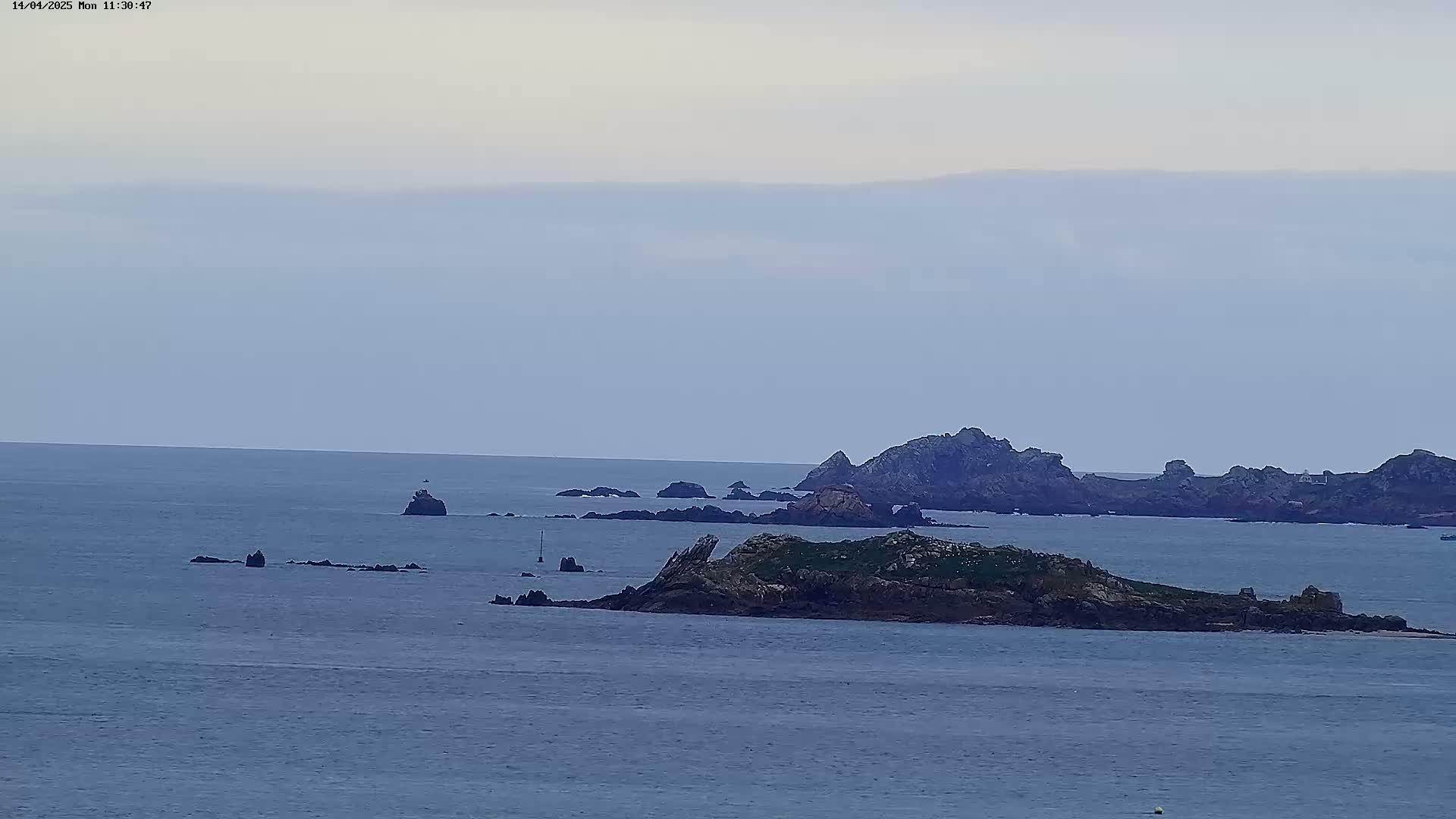 A calm, overcast day reveals a rocky island chain and various smaller outcrops surrounded by a tranquil ocean.