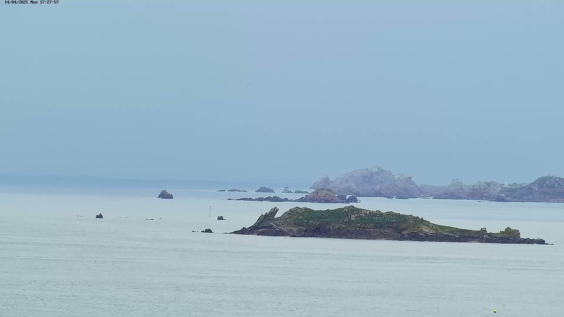 A hazy, overcast day reveals a rocky island and several smaller islets scattered across a calm sea.