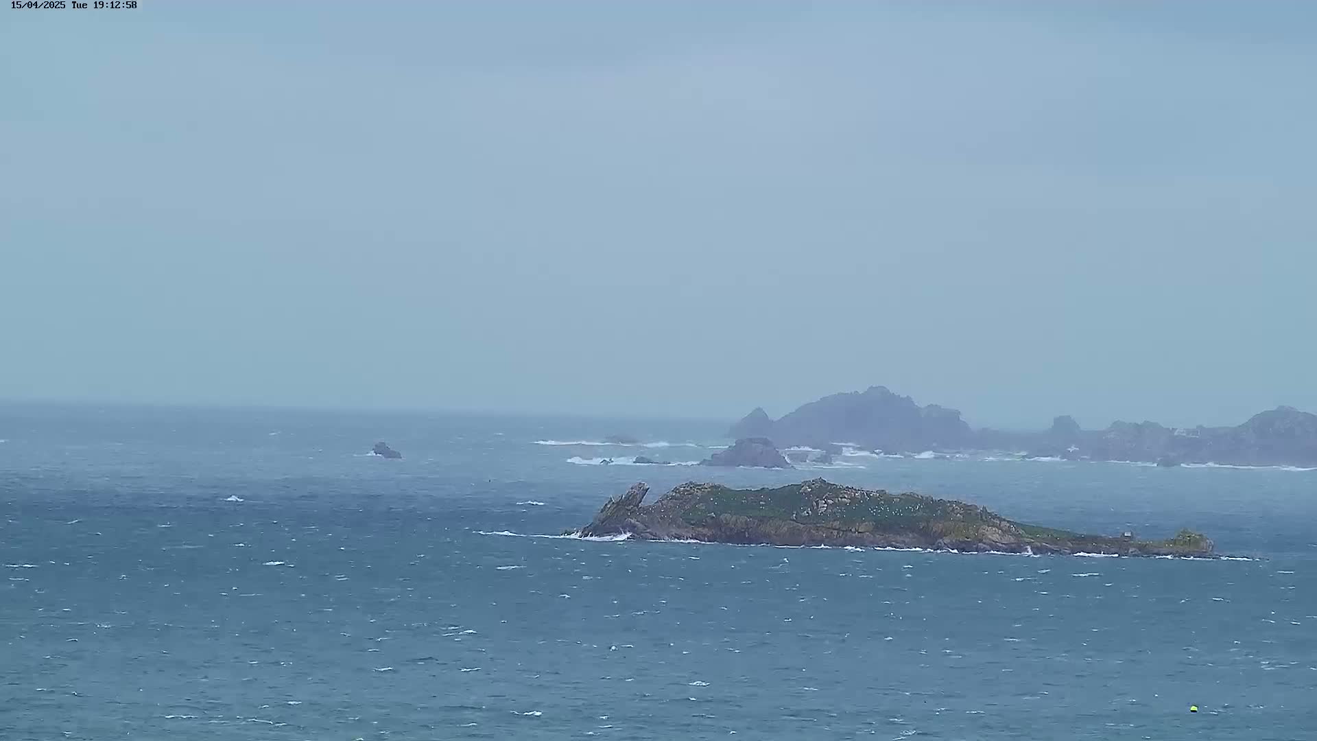 A small, rocky island with sparse vegetation is visible in a choppy sea under an overcast sky.