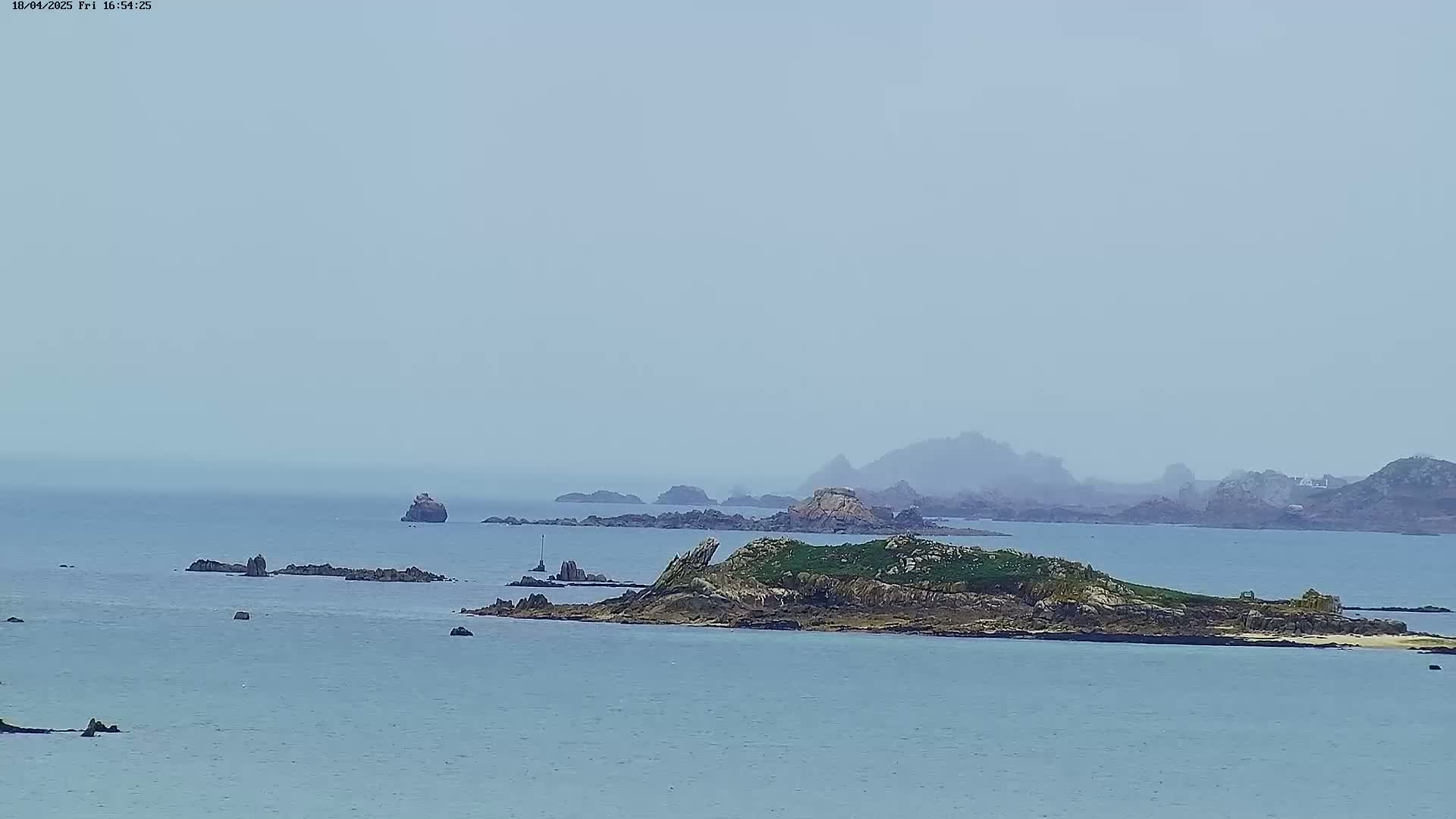 A hazy view of a rocky island and surrounding islets in a calm sea.