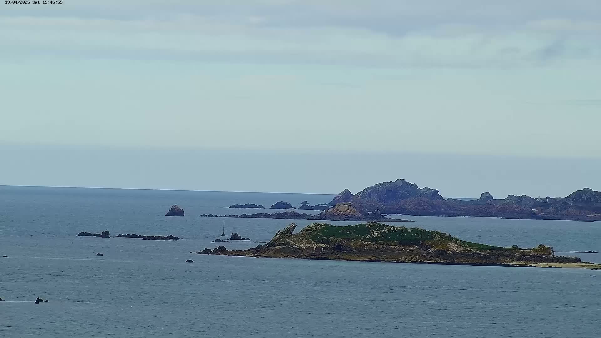 A tranquil ocean scene under a cloudy sky features several small, rocky islands, with one larger island covered in sparse vegetation in the foreground.