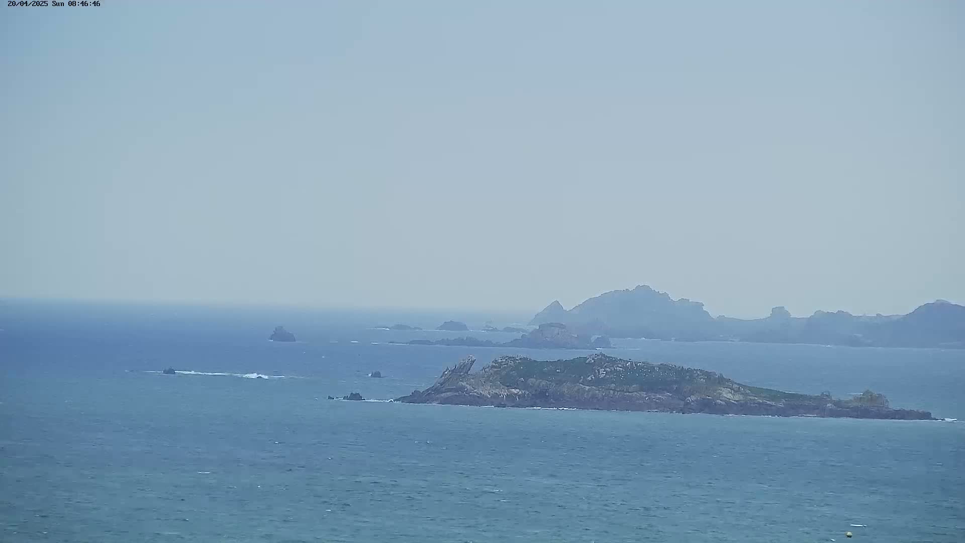 A hazy, distant view shows a rocky island and coastline extending into a calm sea.