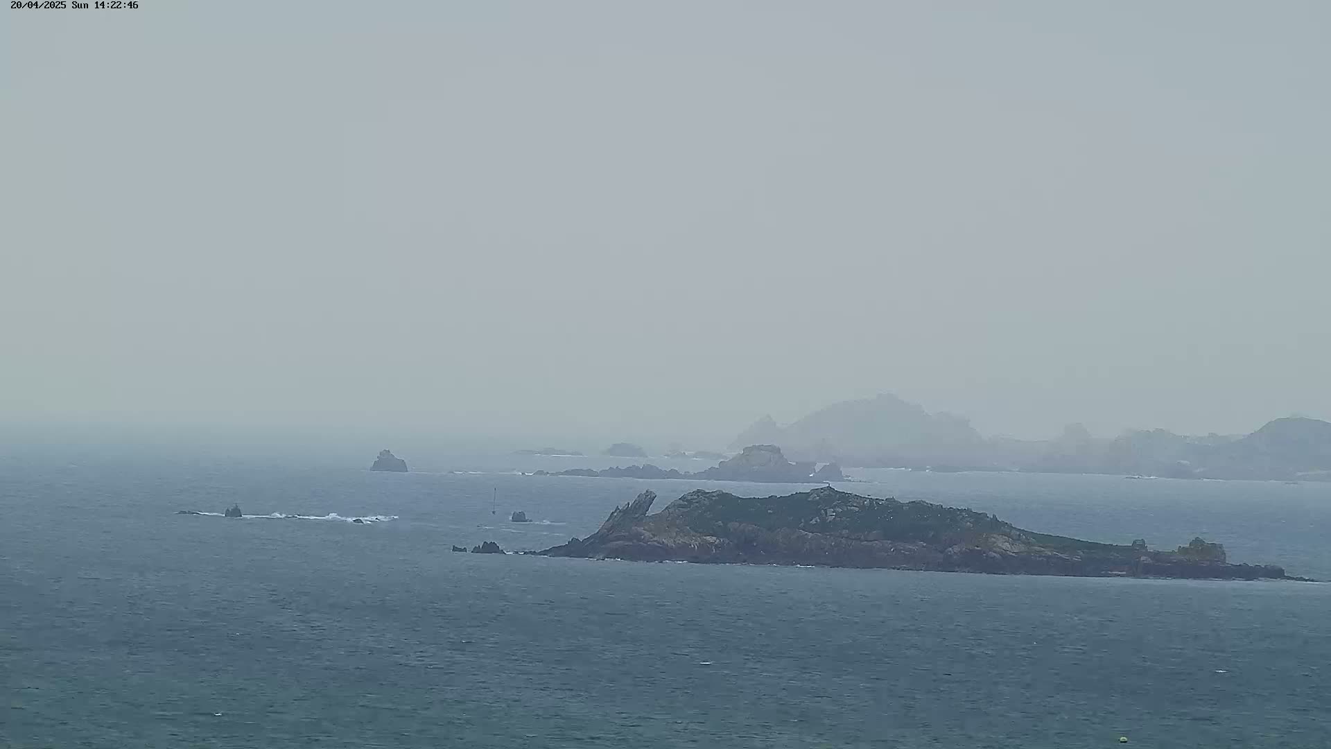 A hazy, overcast day reveals several rocky islands and outcroppings in a calm sea.
