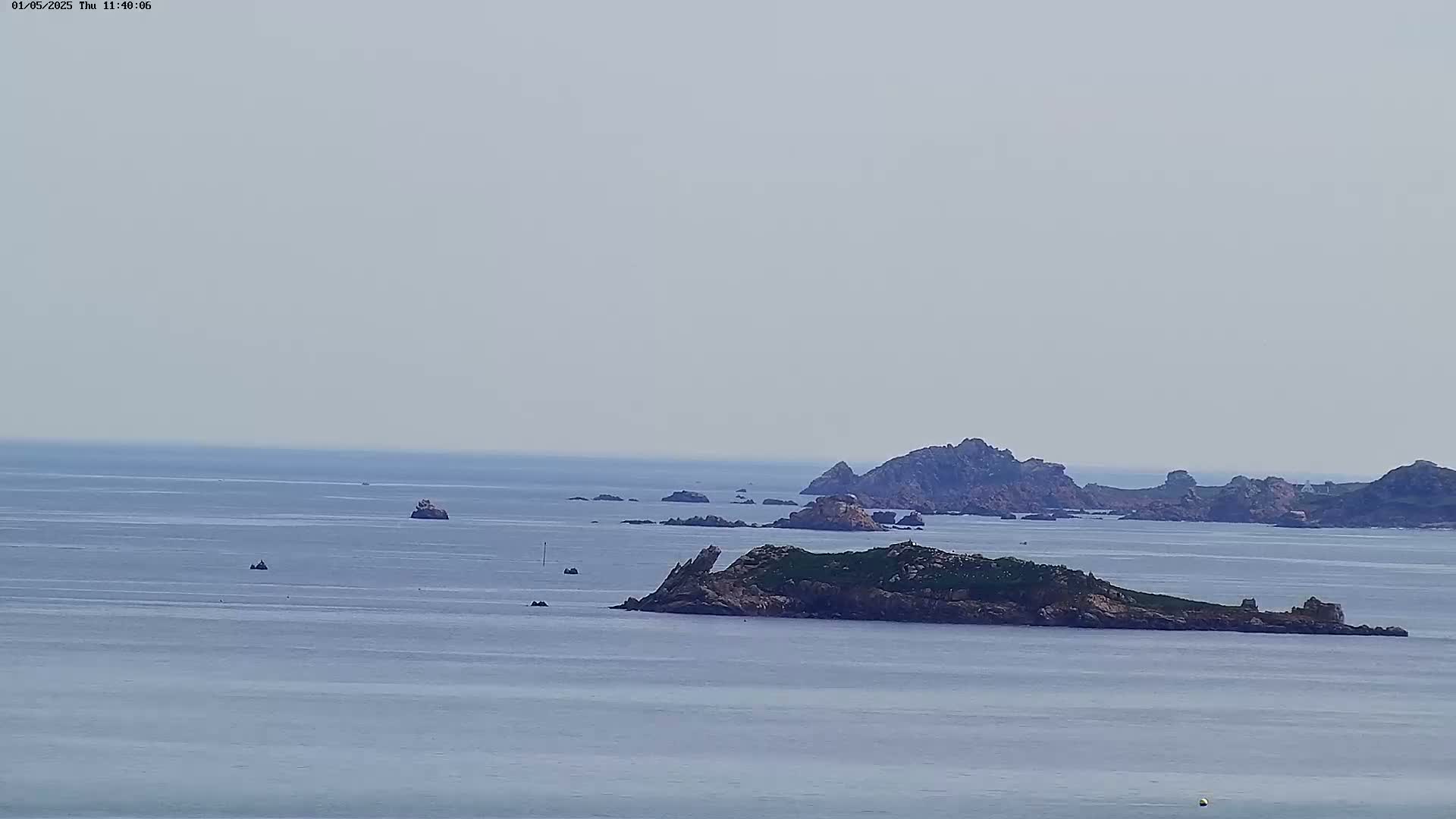 A calm, hazy ocean scene shows several rocky islands and islets scattered across the water.