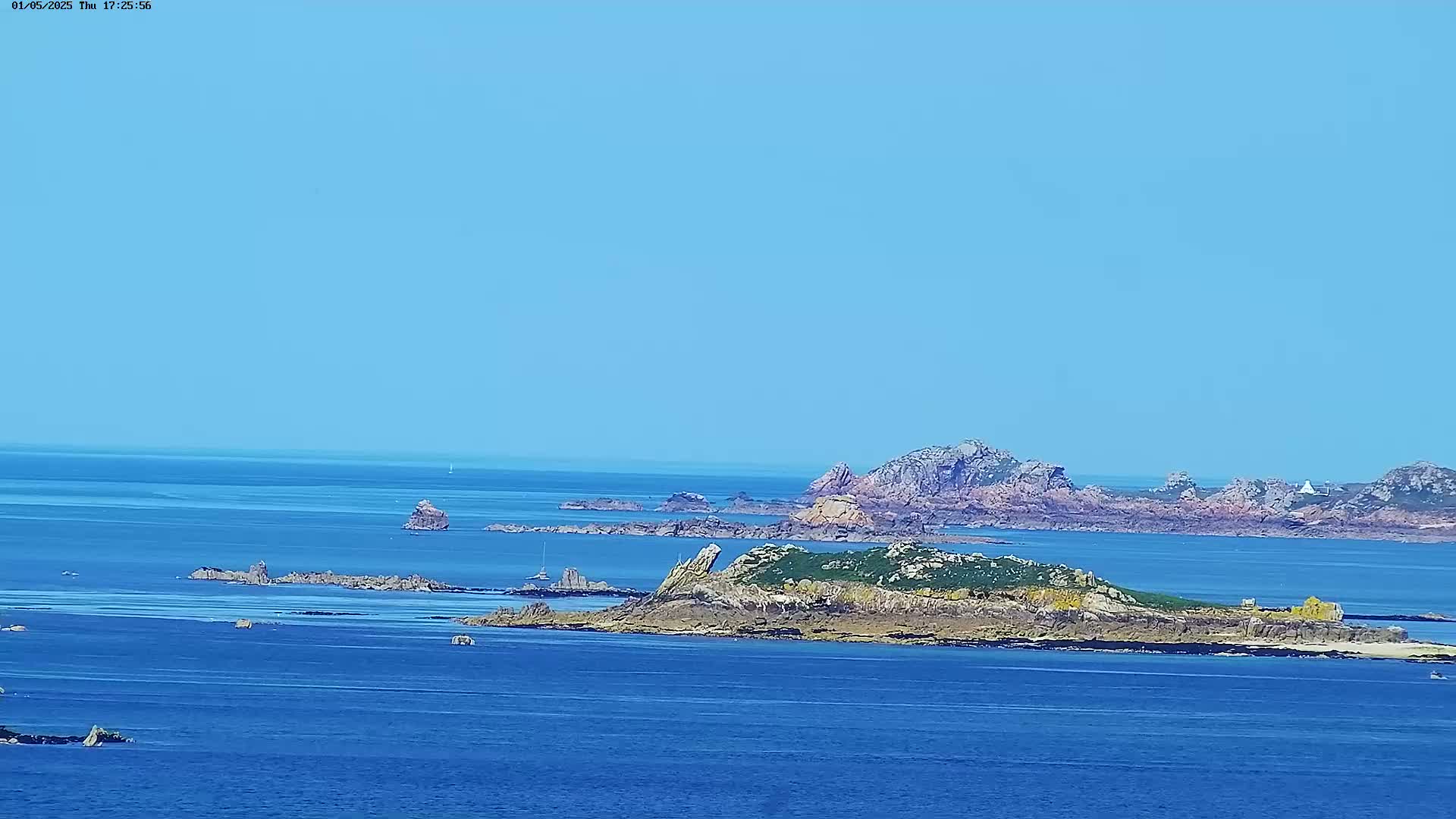 A wide expanse of blue ocean under a clear blue sky features several rocky islands and outcroppings.