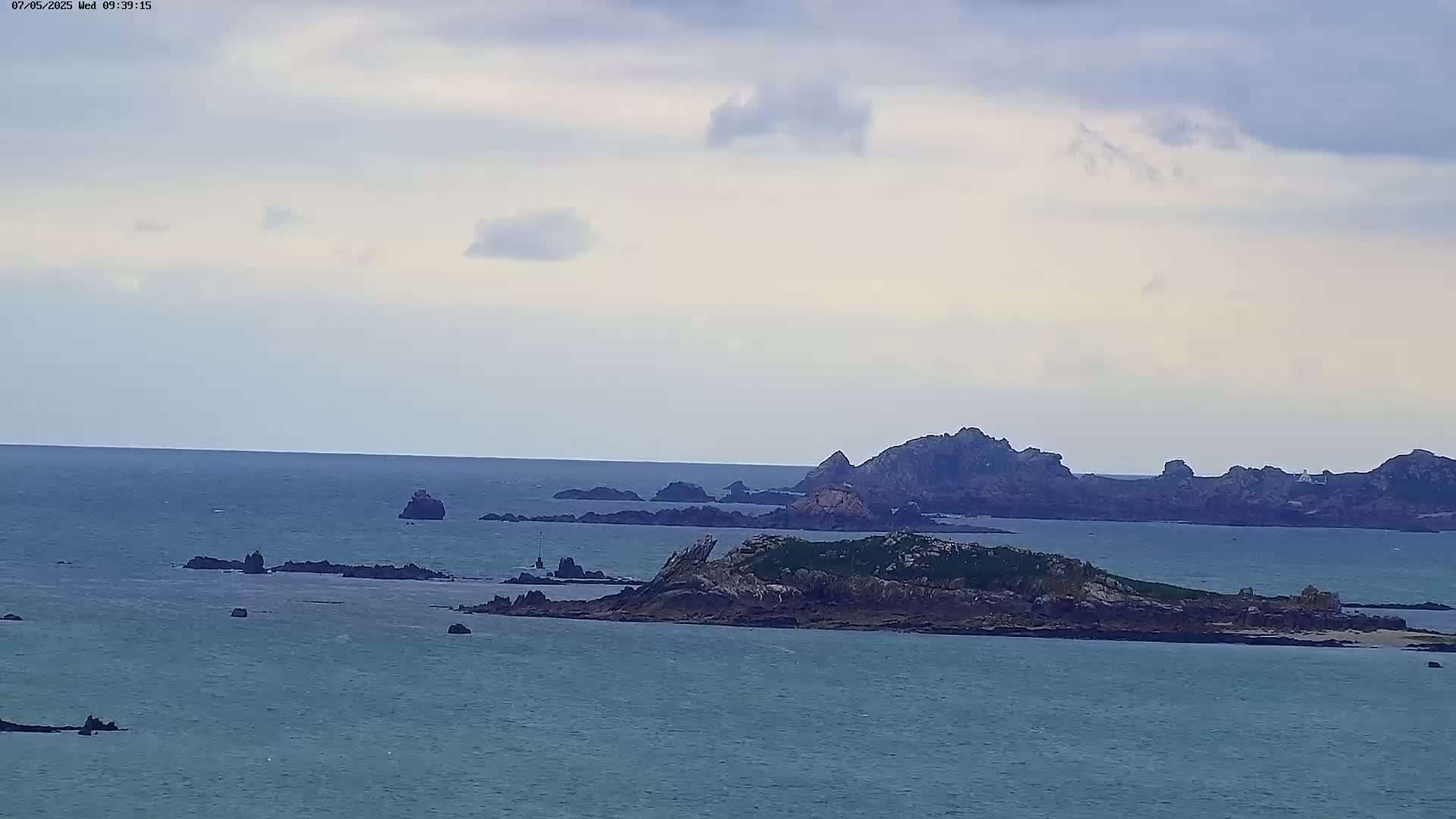 A wide shot of a rocky island chain in a calm sea under a mostly cloudy sky.
