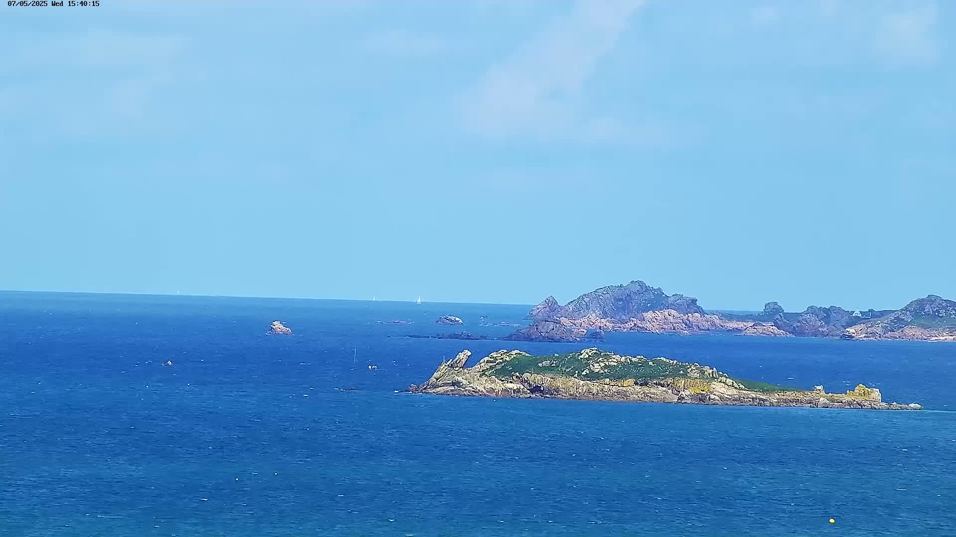 A sunny day reveals a vast expanse of blue ocean dotted with rocky islands and a few distant sailboats.