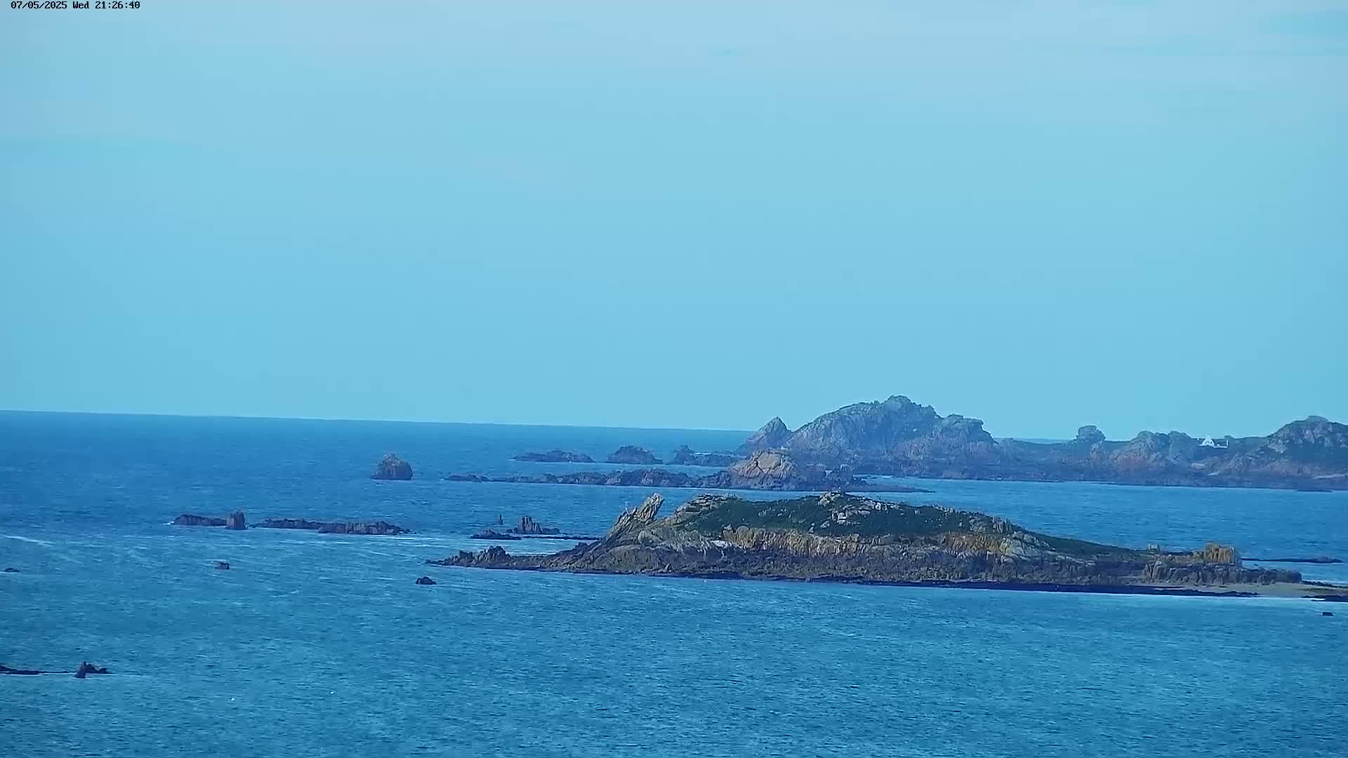 A distant view of rocky islands and a calm blue ocean under a clear sky.