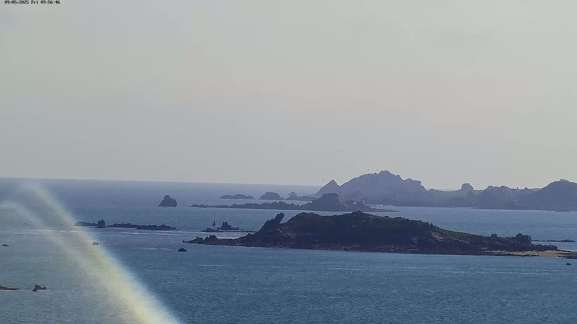 A hazy, distant view of a rocky coastline and several small islands in a calm sea.