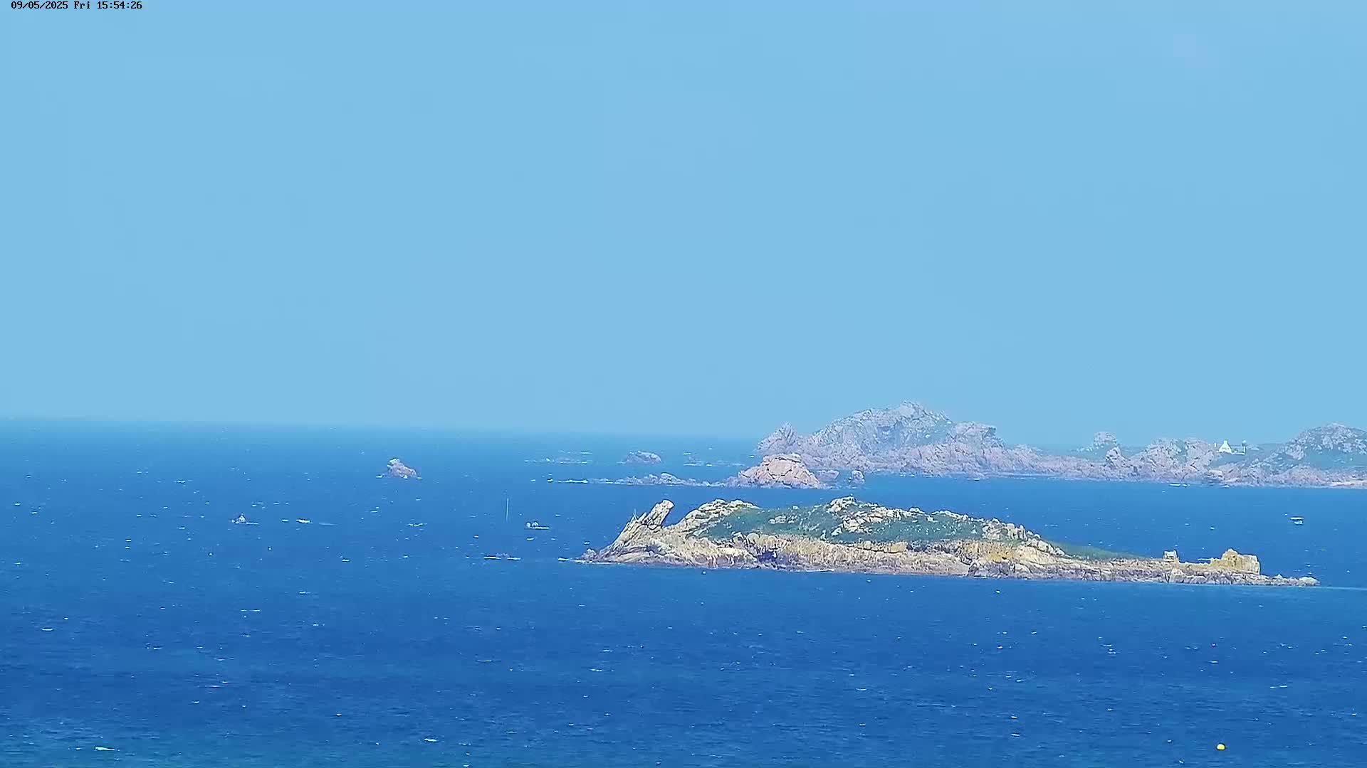A rocky island, surrounded by a calm, blue ocean under a clear, light-blue sky, is visible from a distance.