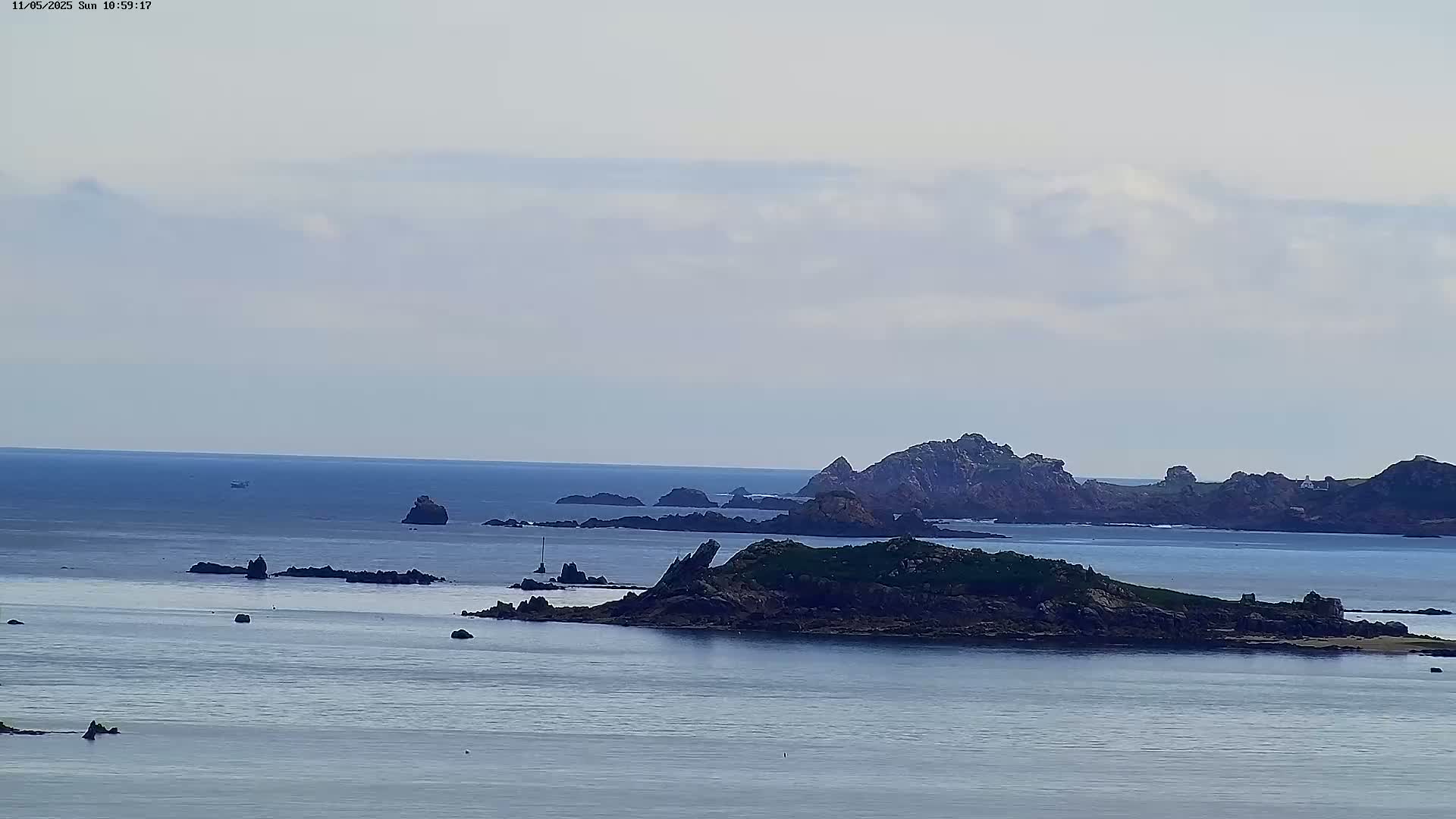A calm, overcast day reveals a vast expanse of ocean dotted with numerous rocky islands and a lone boat in the distance.
