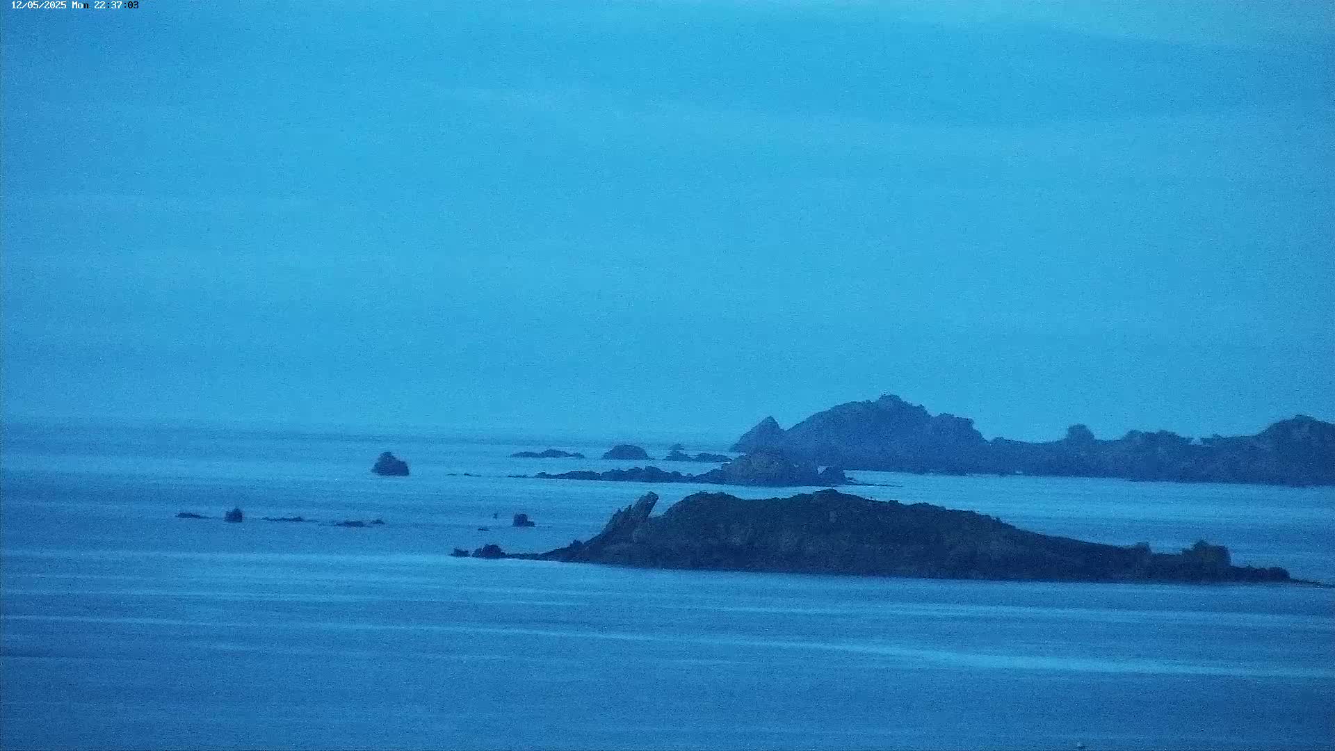 Dark, rocky islands are scattered across a calm, blue sea under a clear, twilight sky.